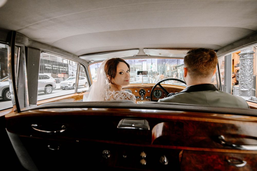 Bride and groom riding in a vintage classic wedding car, bride looking back elegantly in her veil.