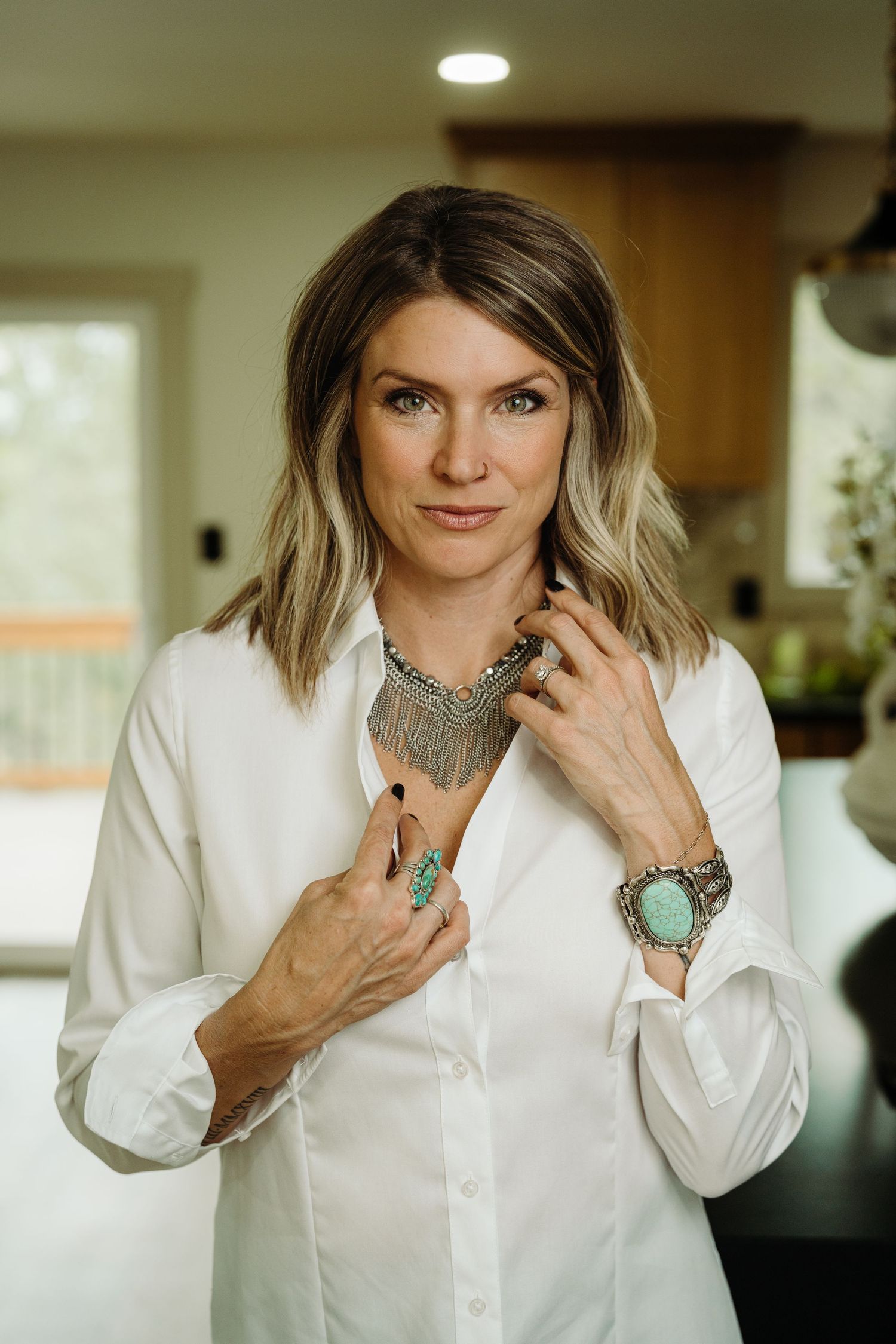 Woman in white button-up shirt wearing turquoise jewelry, posing indoors with a confident smile.