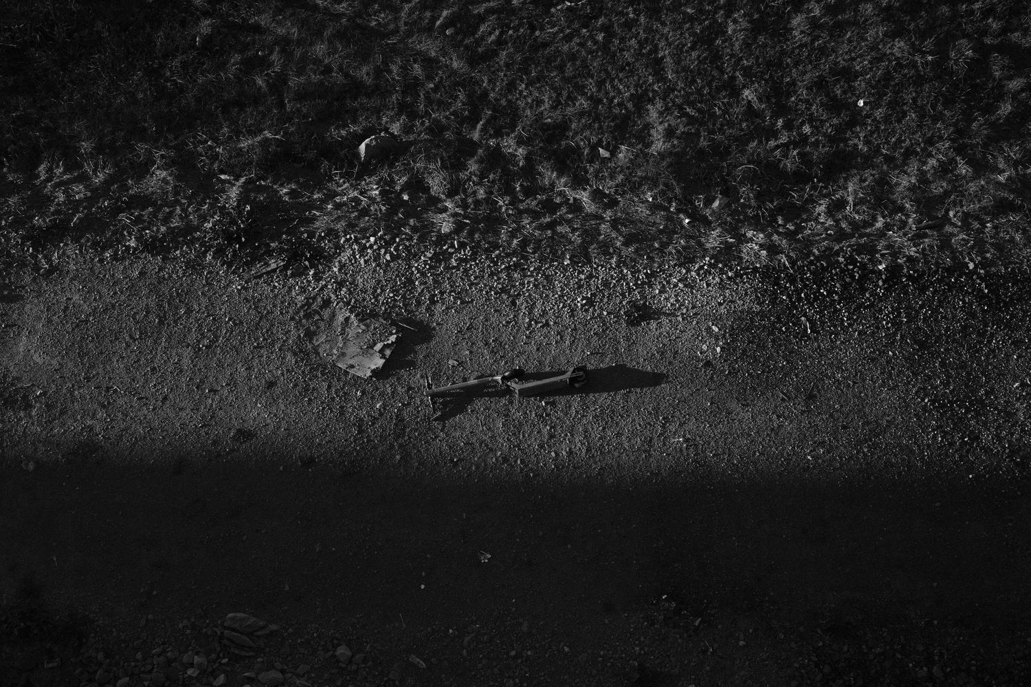 Dark moody black and white photo of a small twig casting a shadow on wet pavement at night.