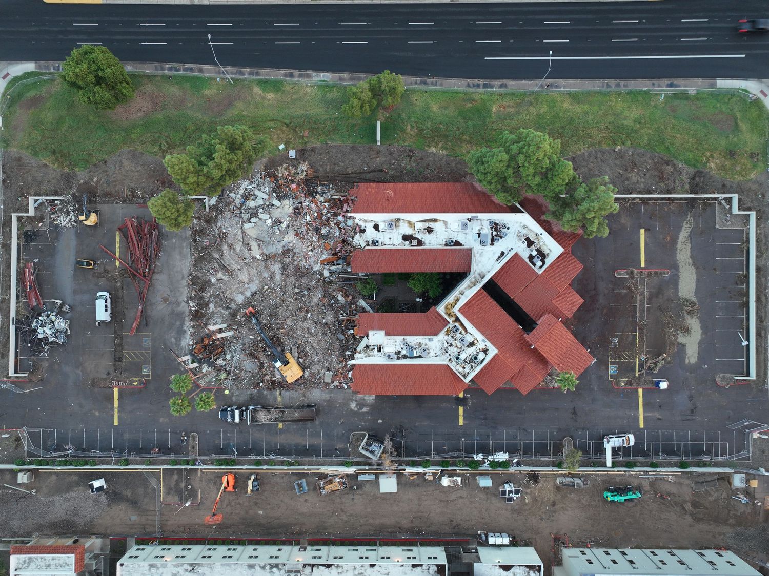 Aerial drone view of a partially demolished building with red roof and rubble in a parking lot.