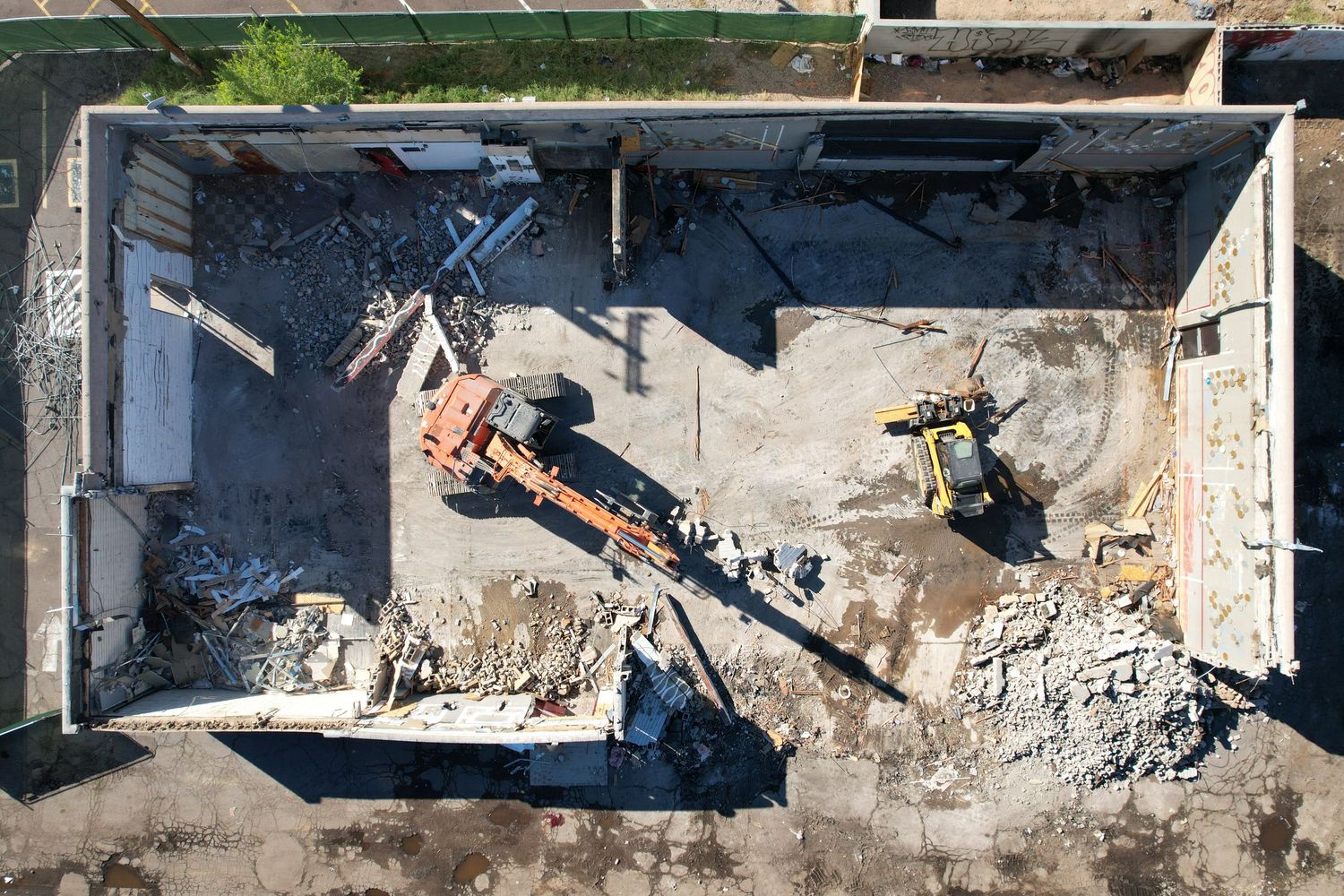 Aerial view of a building demolition site with excavator machinery clearing rubble and debris from a concrete structure.