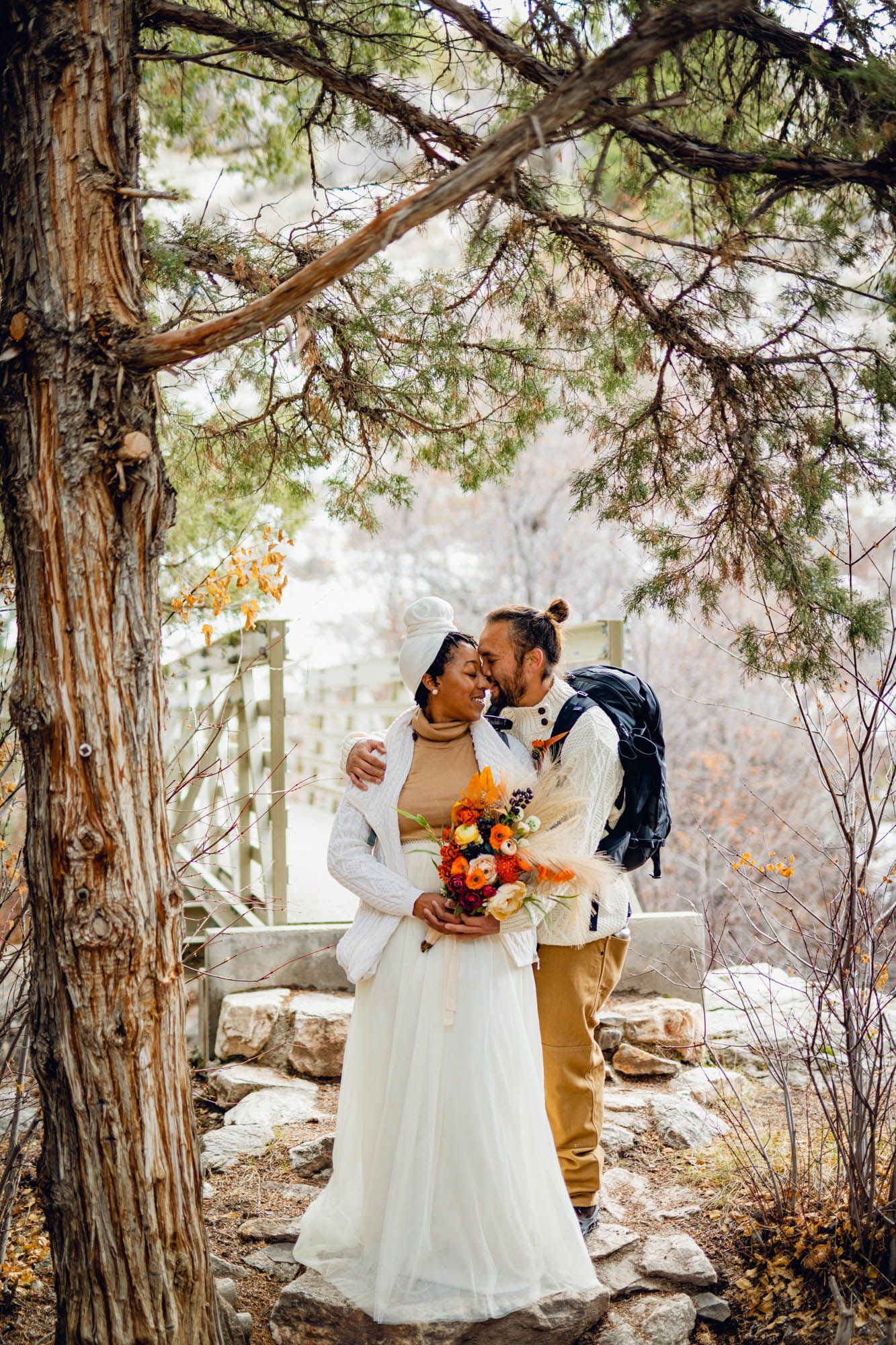 Bride and groom share a romantic moment under pine trees, colorful autumn bouquet in snowy outdoor setting. Idaho Hot Springs Elopement.