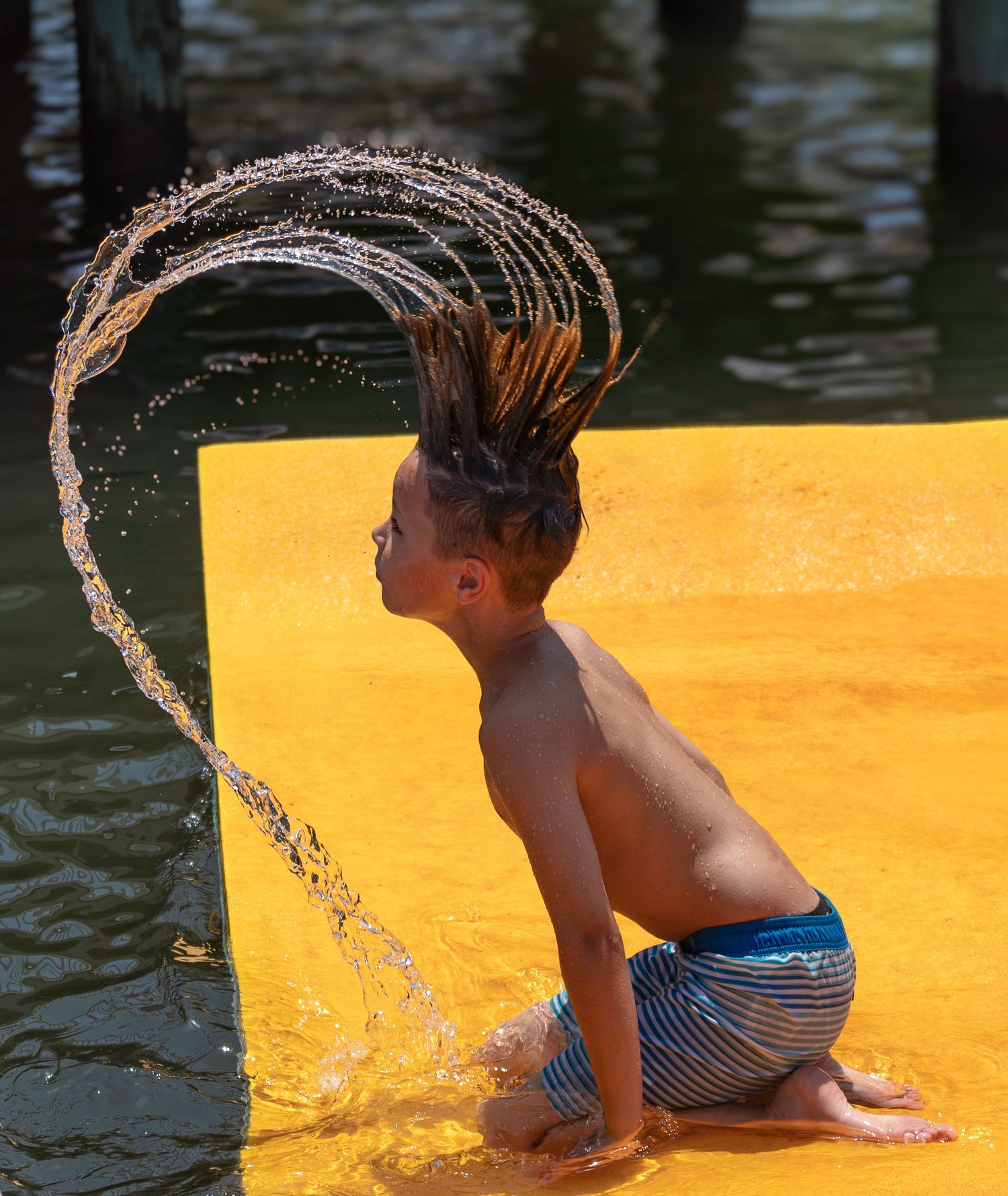 Boy plays in the bay and throws wet hair into the air.