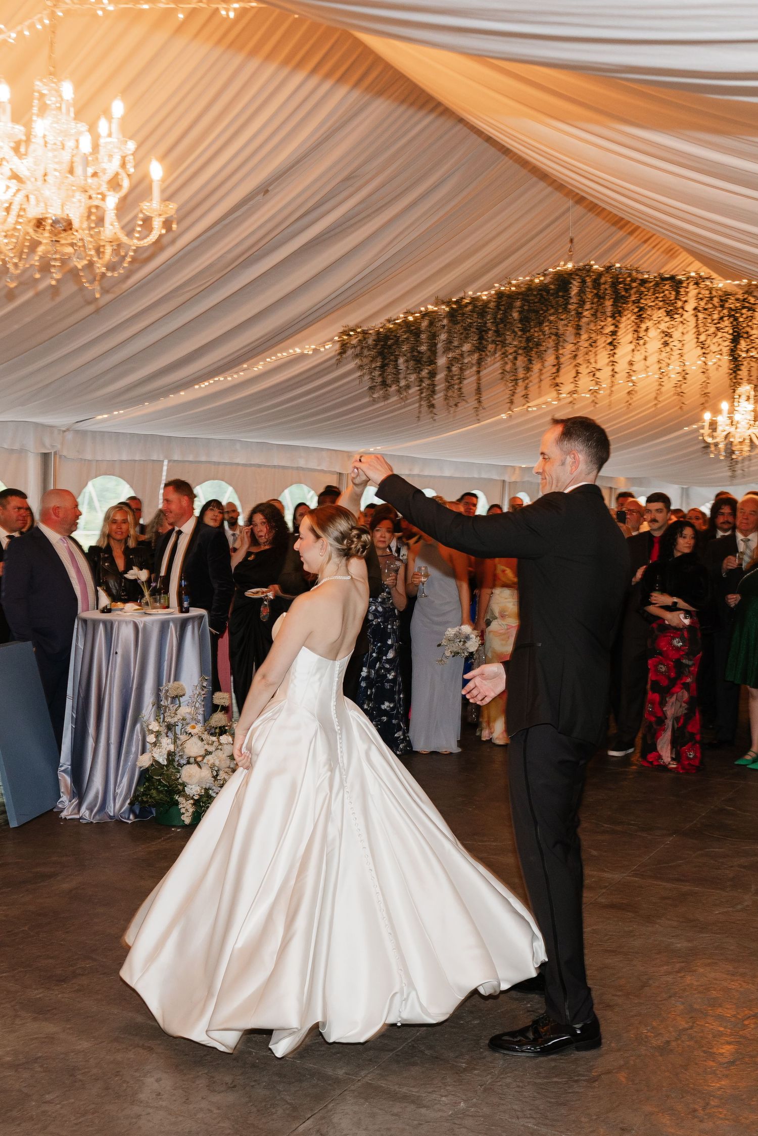 Groom spins bride in a stunning white ballgown during their first dance at wedding reception.