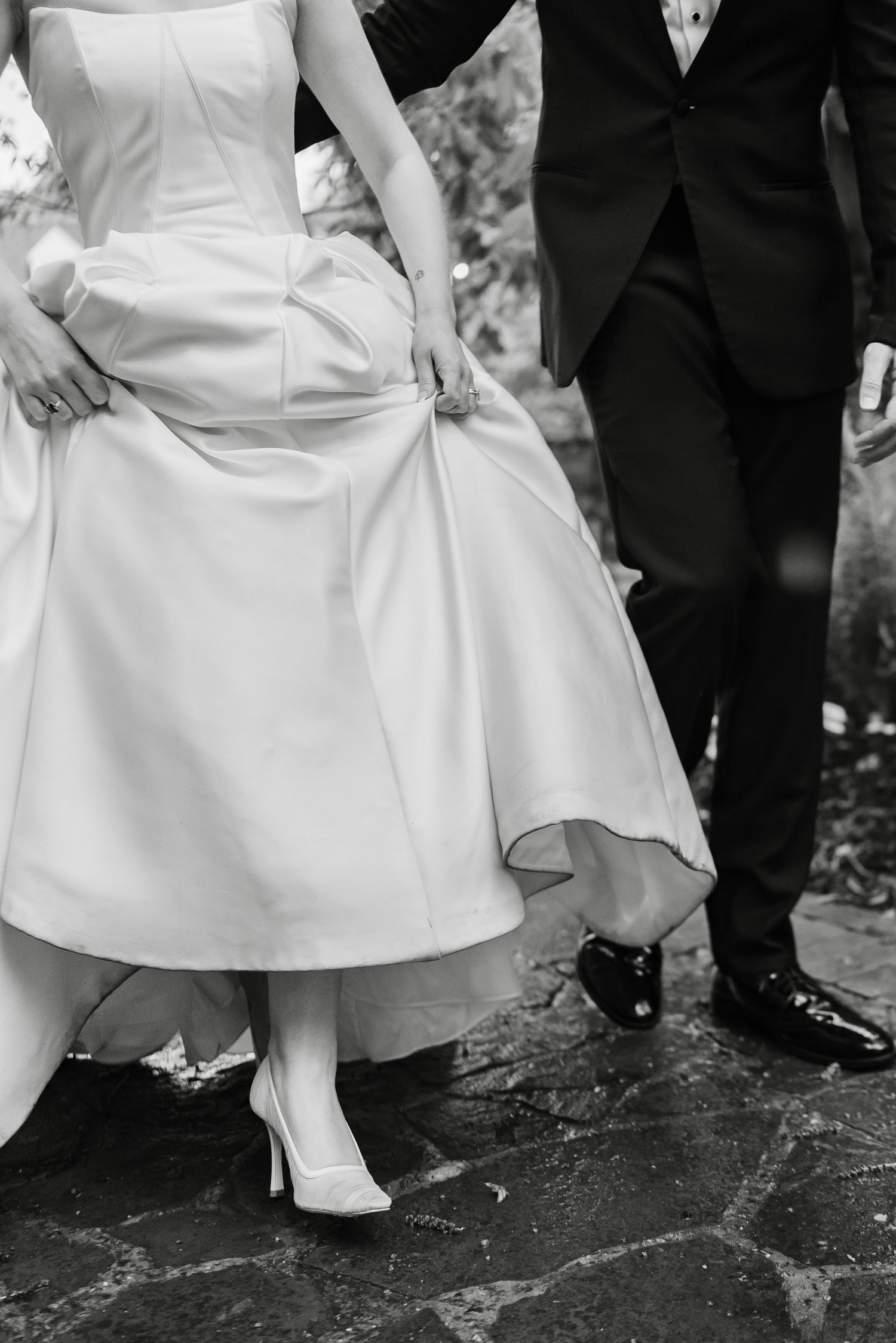 Black and white detail shot of bride in ball gown and groom walking on stone path.