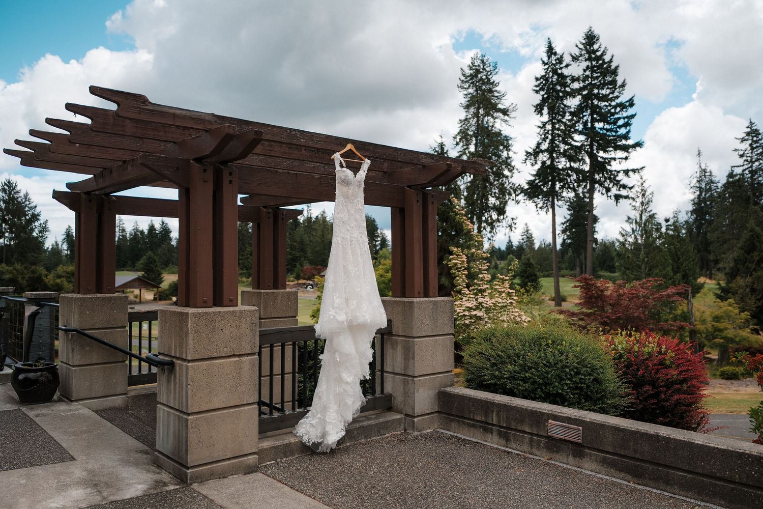 Elegant white wedding dress hanging from a wooden pergola outdoors at McCormick Woods Golf Club for Mayella and Andrey's wedding.