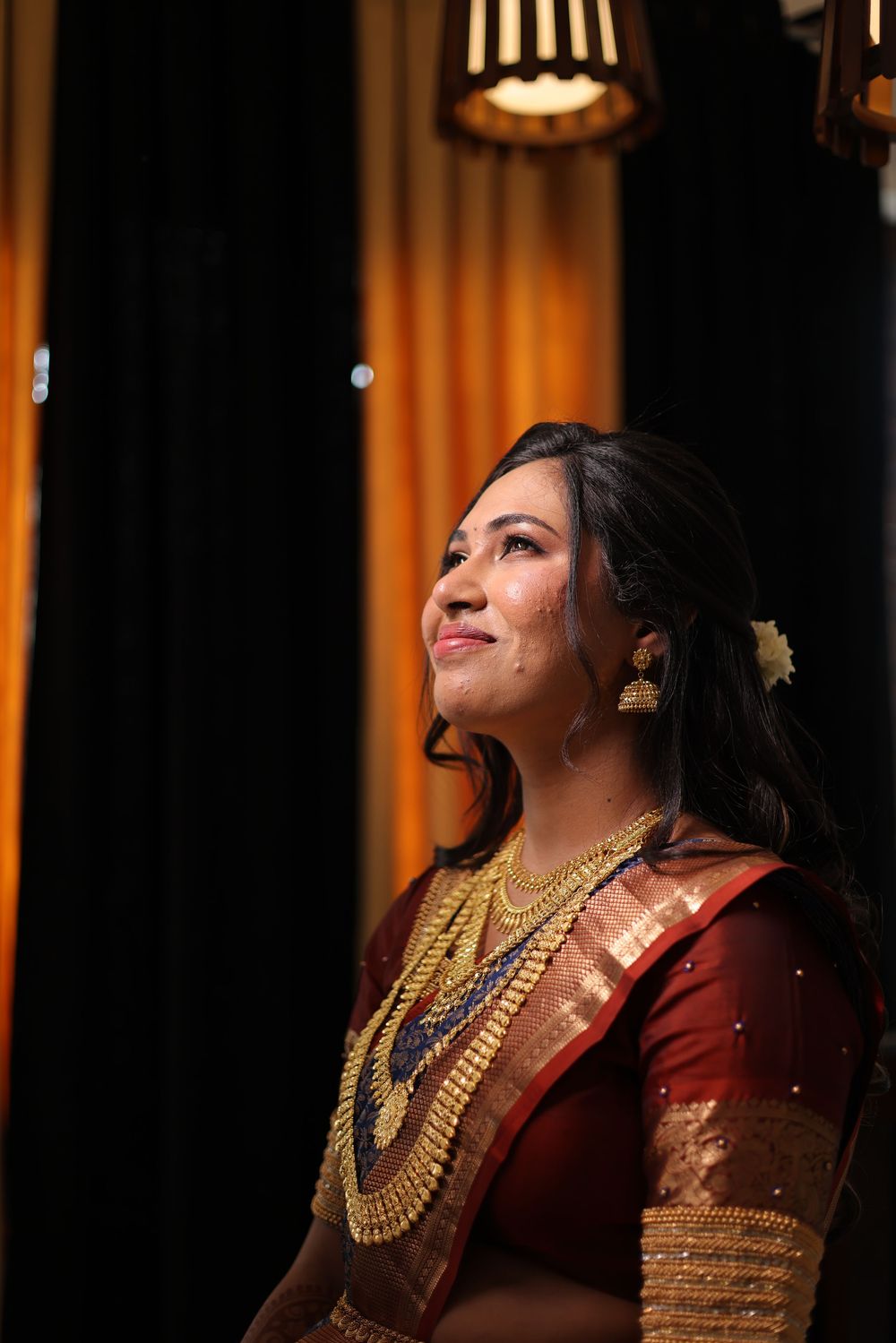 South Indian bride in red silk saree with gold jewelry smiling gracefully under warm lighting.