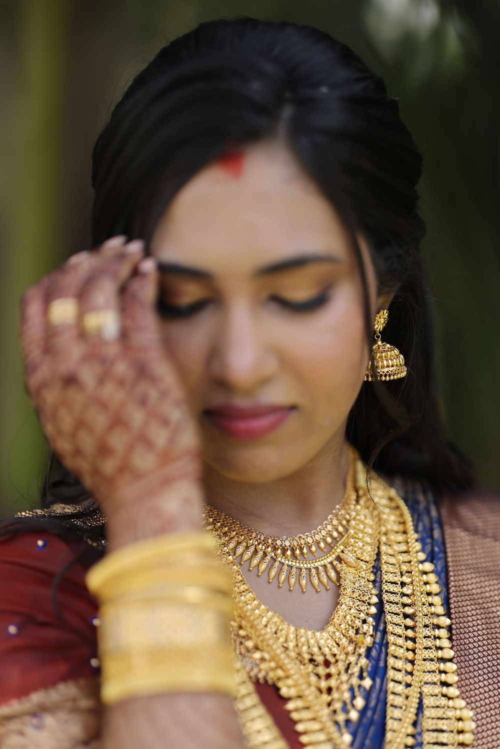 Indian bride adorned in gold jewelry and mehndi, wearing traditional necklaces and earrings with a red bindi.
