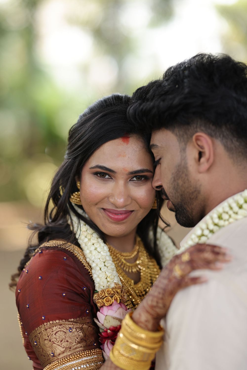 Indian bride and groom in traditional wedding attire with gold jewelry and floral garlands sharing an intimate moment.