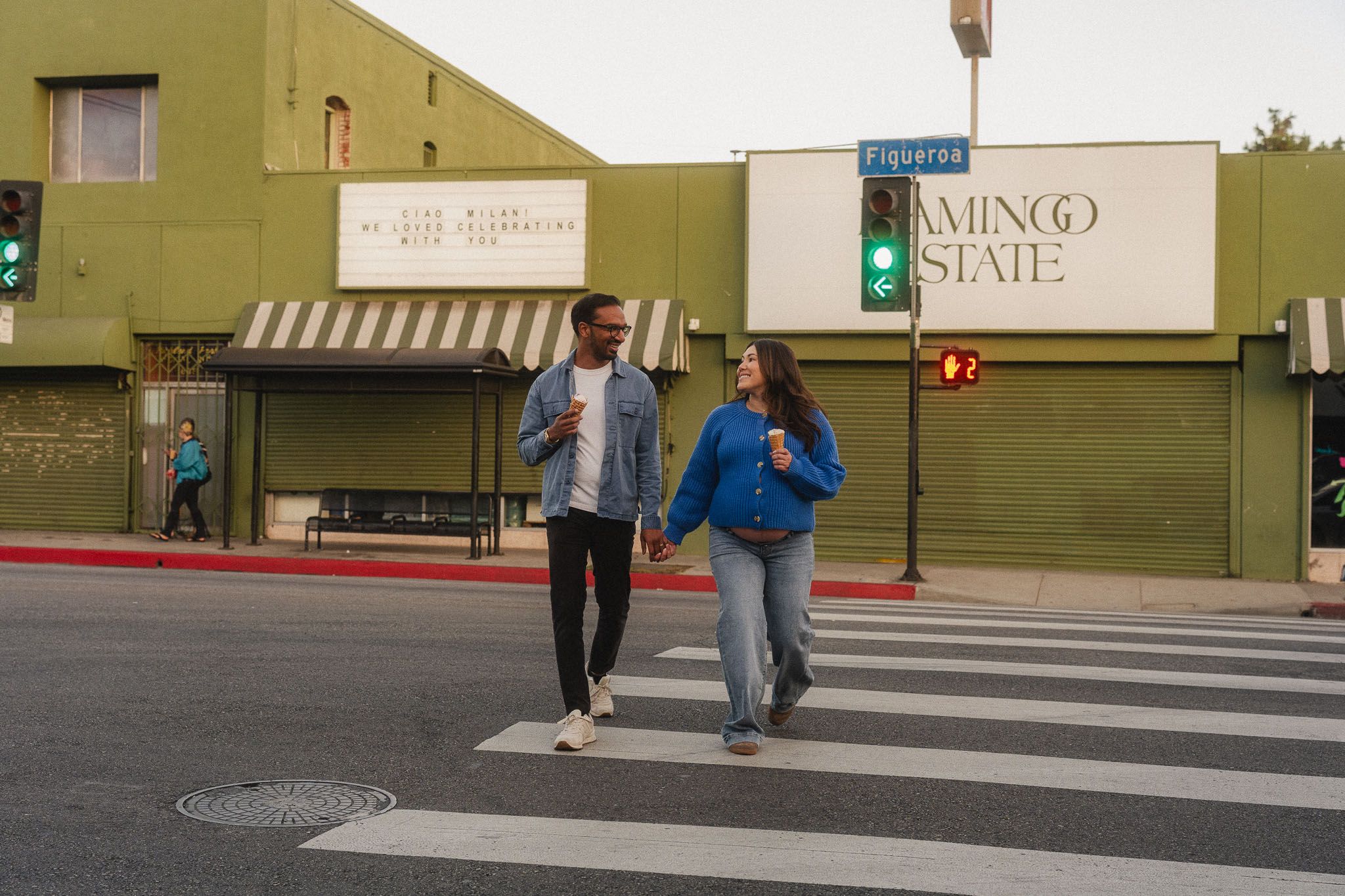 Amanda and Rohan walking across a Pasadena street with ice cream during their maternity date night photoshoot
