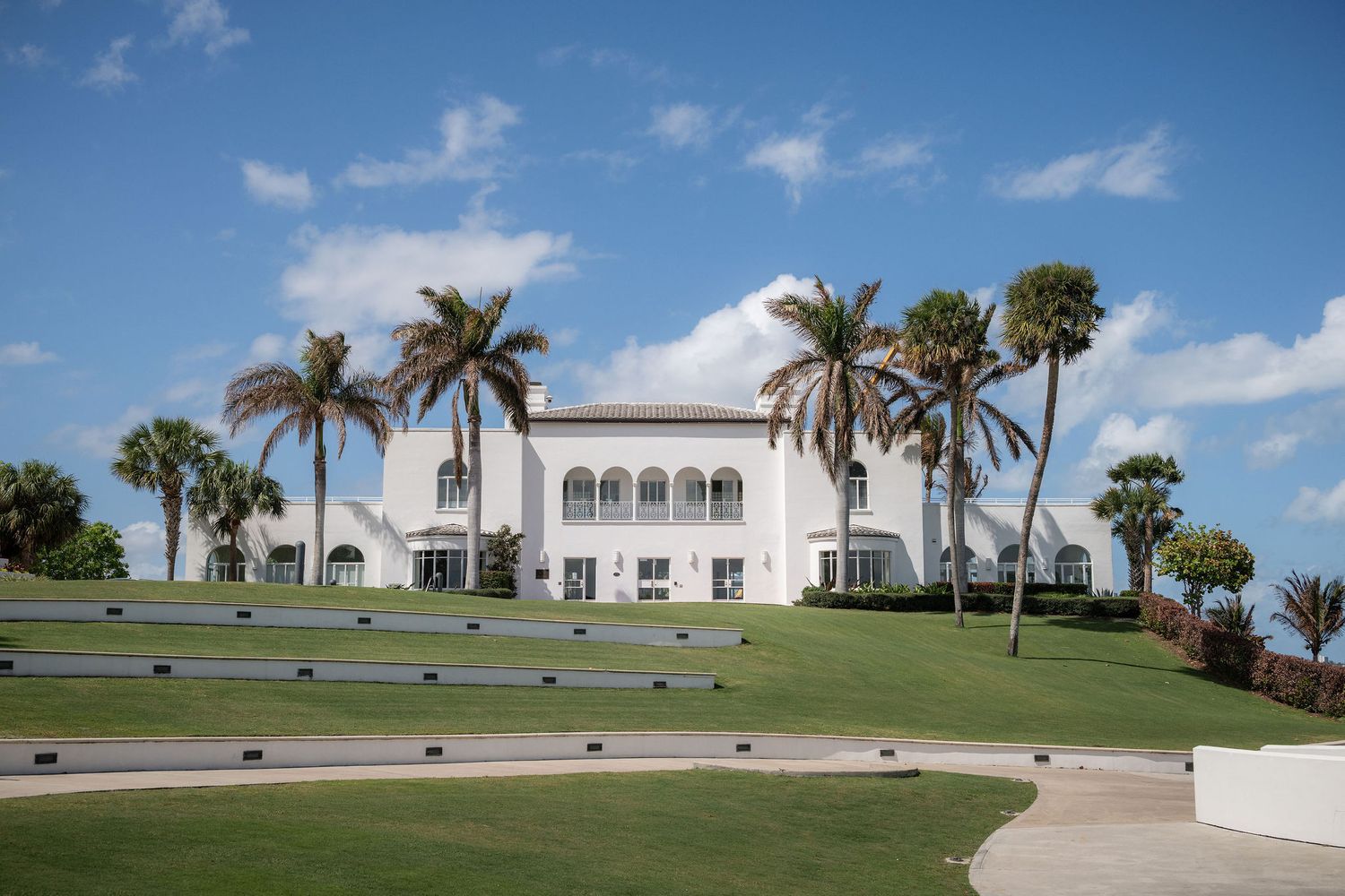 The Mansion at Tuckahoe in Jensen Beach, Florida, seen across the sloping lawn with palm trees framing the white Mediterranean rev