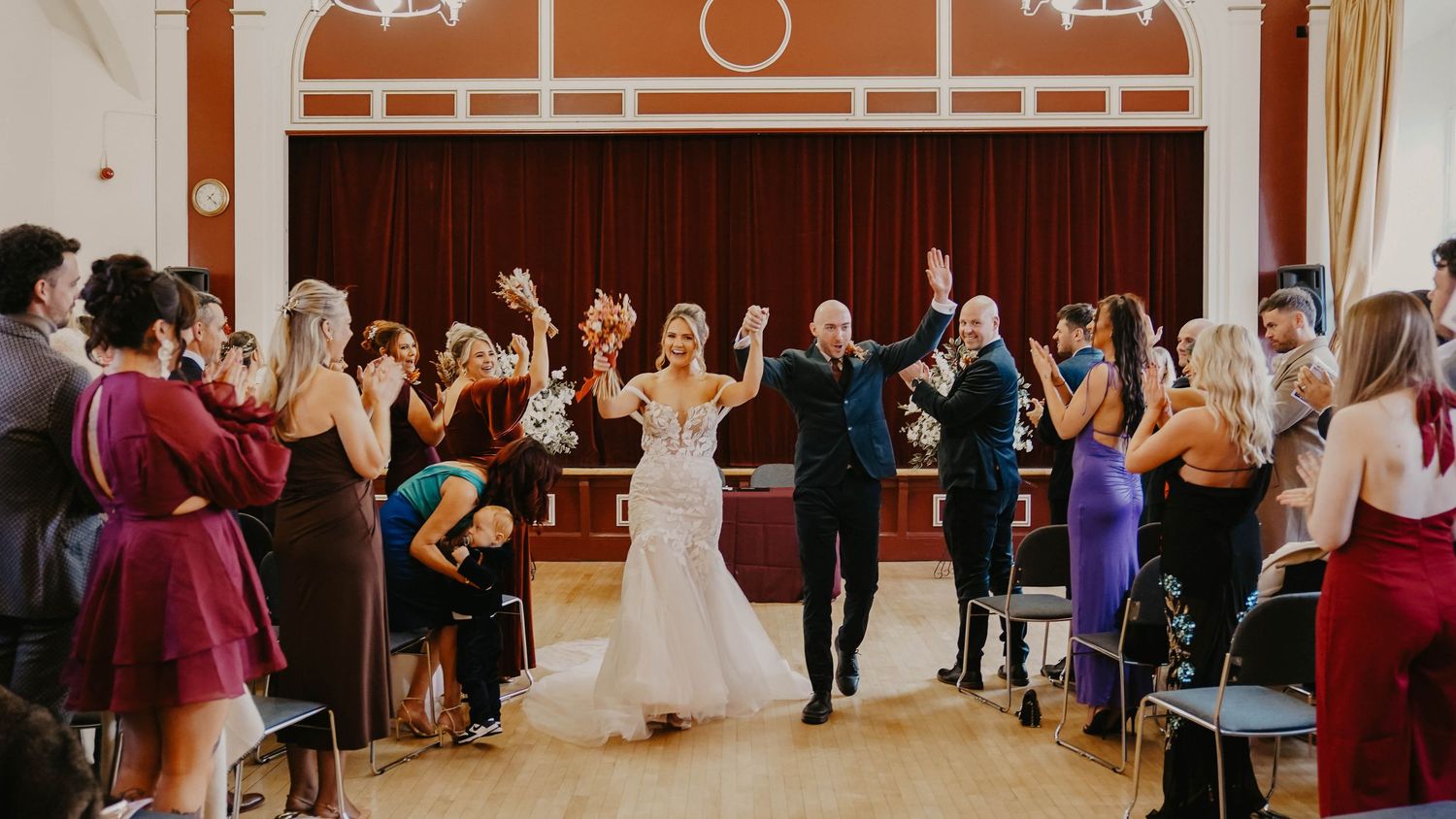 Bride and groom walk triumphantly down the aisle at their wedding reception in an elegant ballroom.