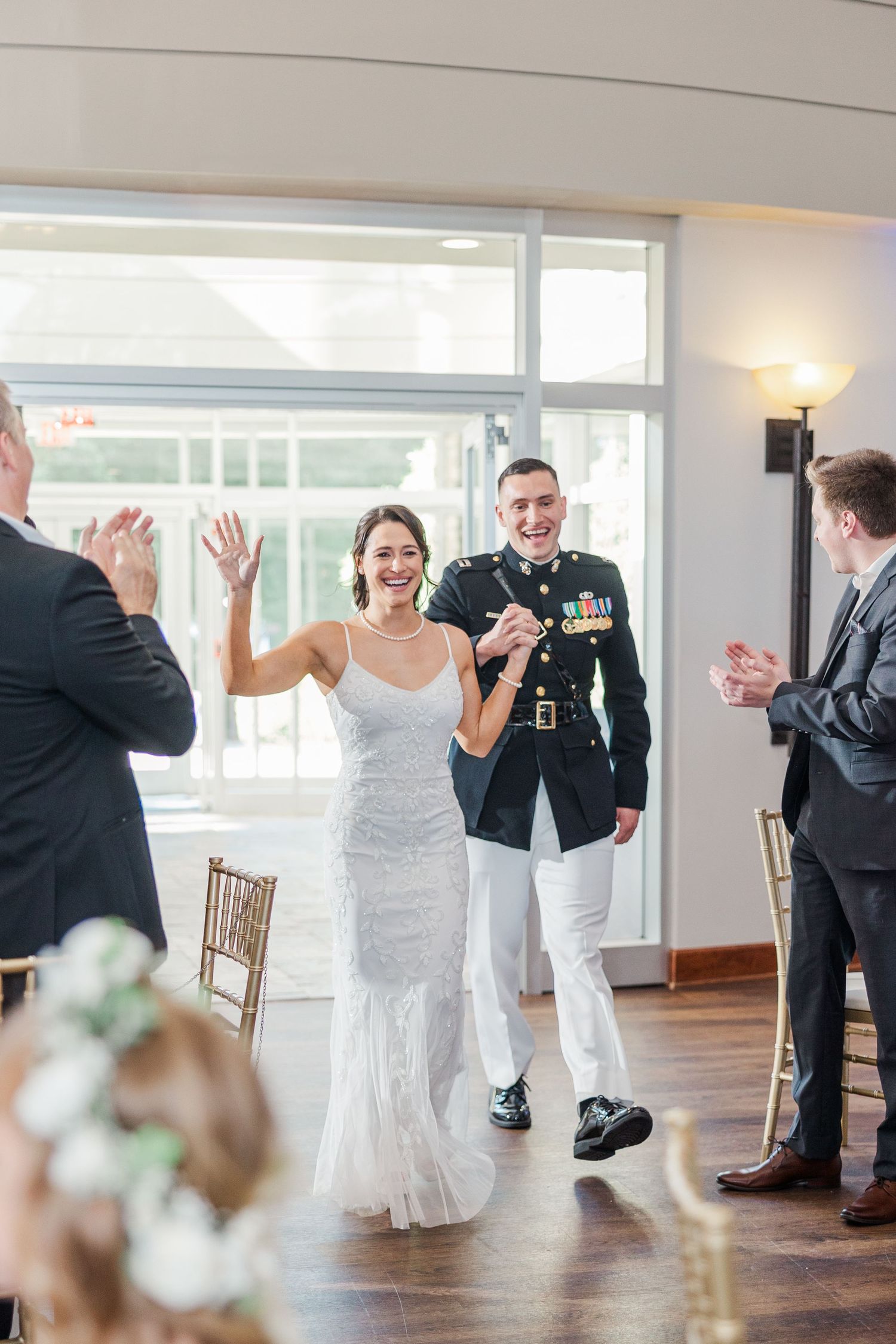 A joyful bride in a white gown and groom in military dress uniform make their grand reception entrance.