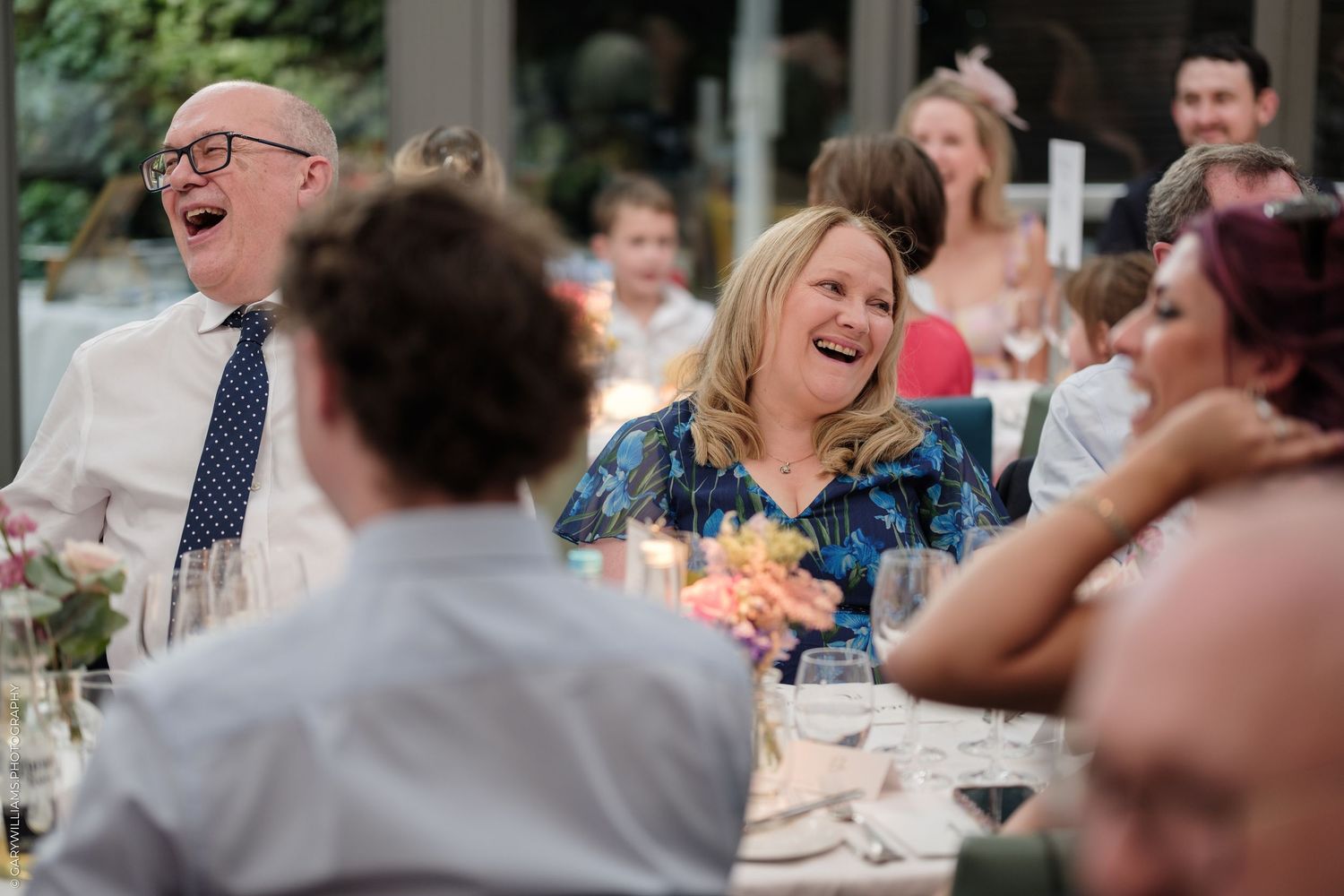 Guests laughing joyfully at a wedding reception dinner, seated at an elegantly decorated table.