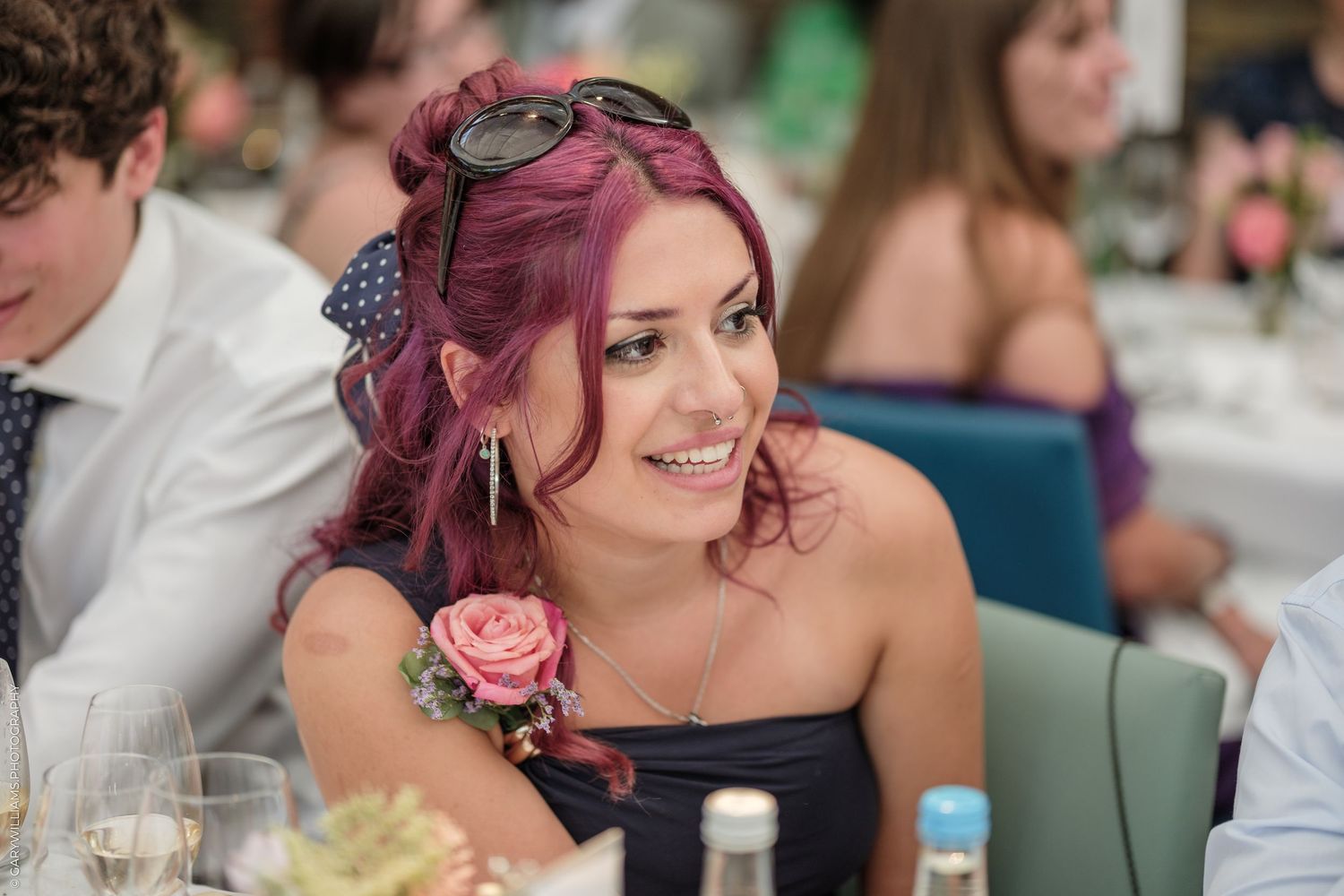 Smiling woman with pink hair and floral corsage at an elegant wedding reception dinner.