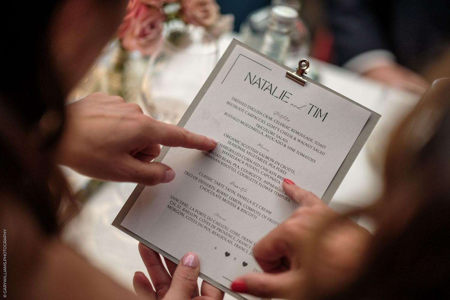 Hands holding a wedding menu card for Natalie and Tim at an elegant reception table.