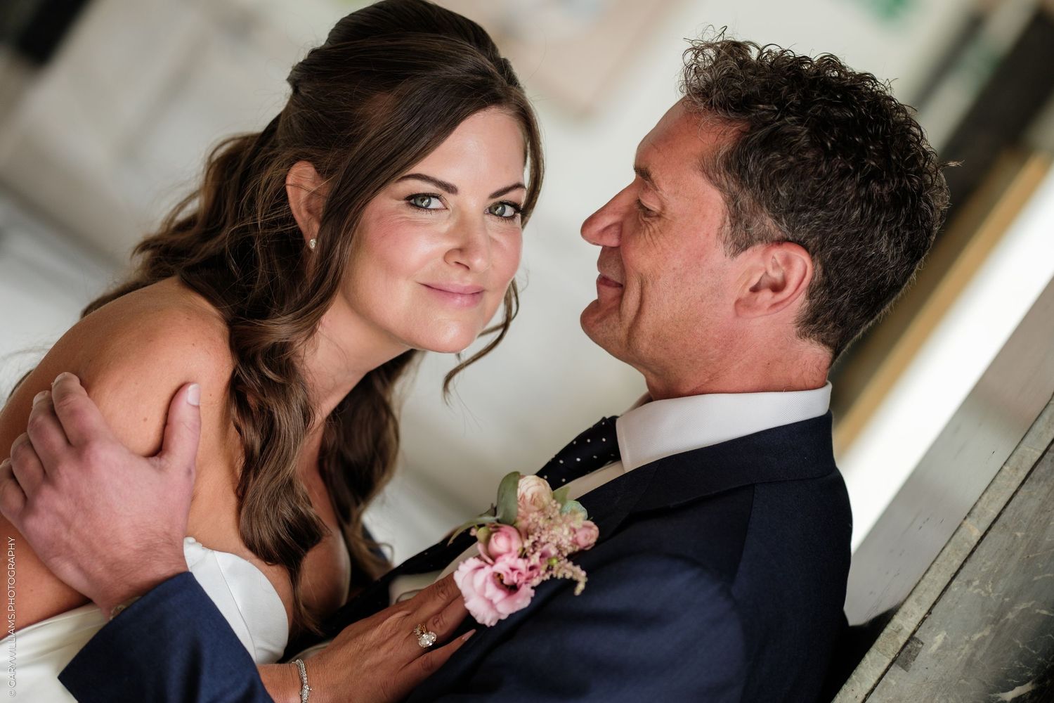 A bride and groom share a romantic moment, smiling at each other, with the groom wearing a boutonniere at their wedding.