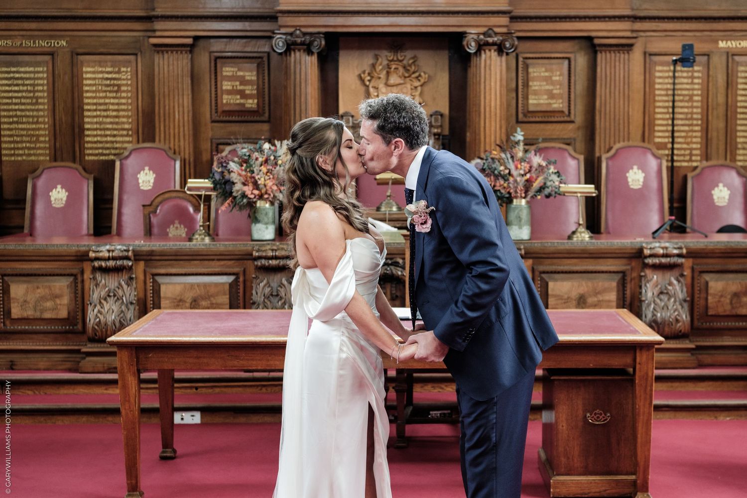 Bride and groom share first kiss at ornate wooden altar during elegant wedding ceremony.