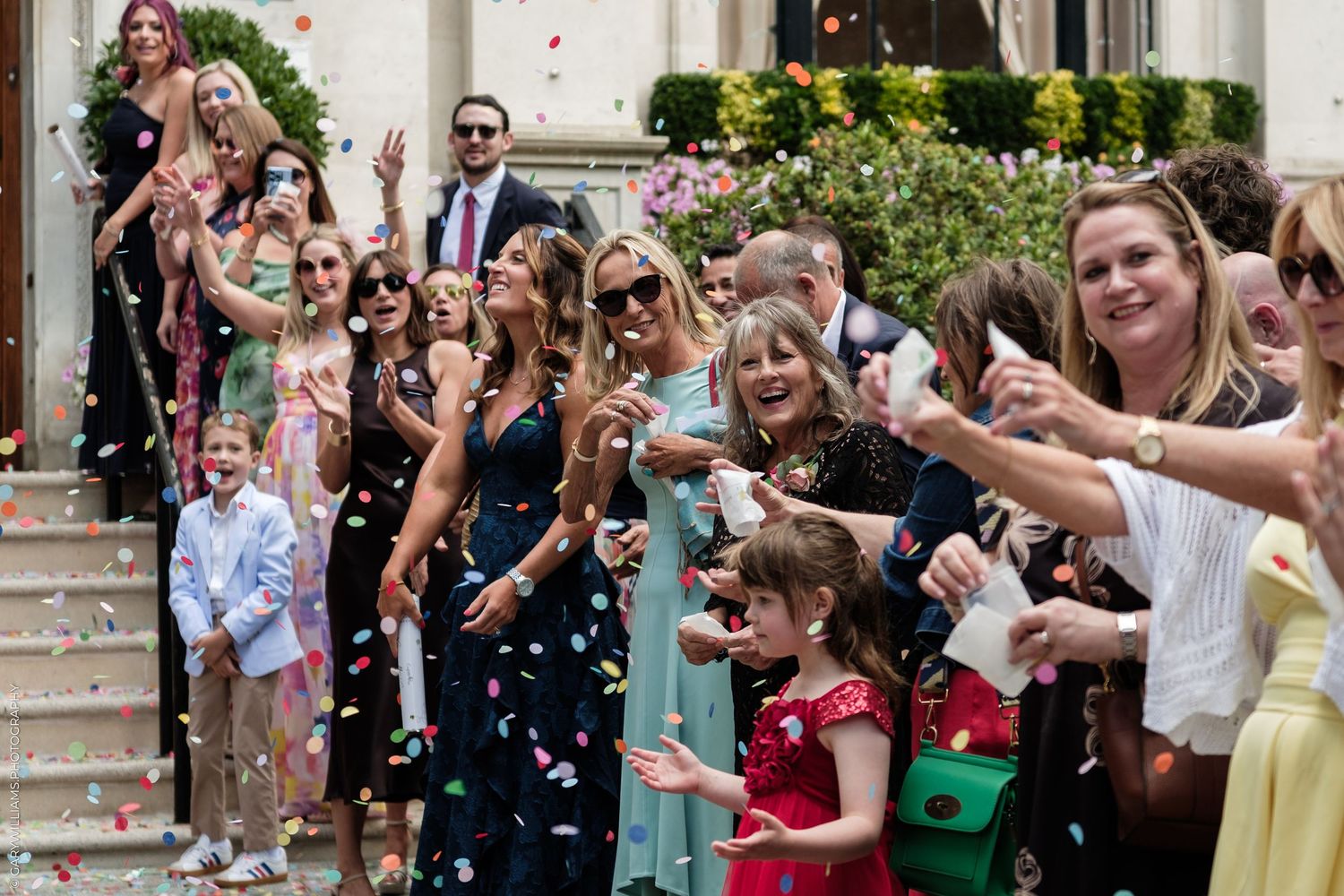 Joyful wedding guests tossing colorful confetti outside a venue, celebrating the newlyweds in elegant attire.