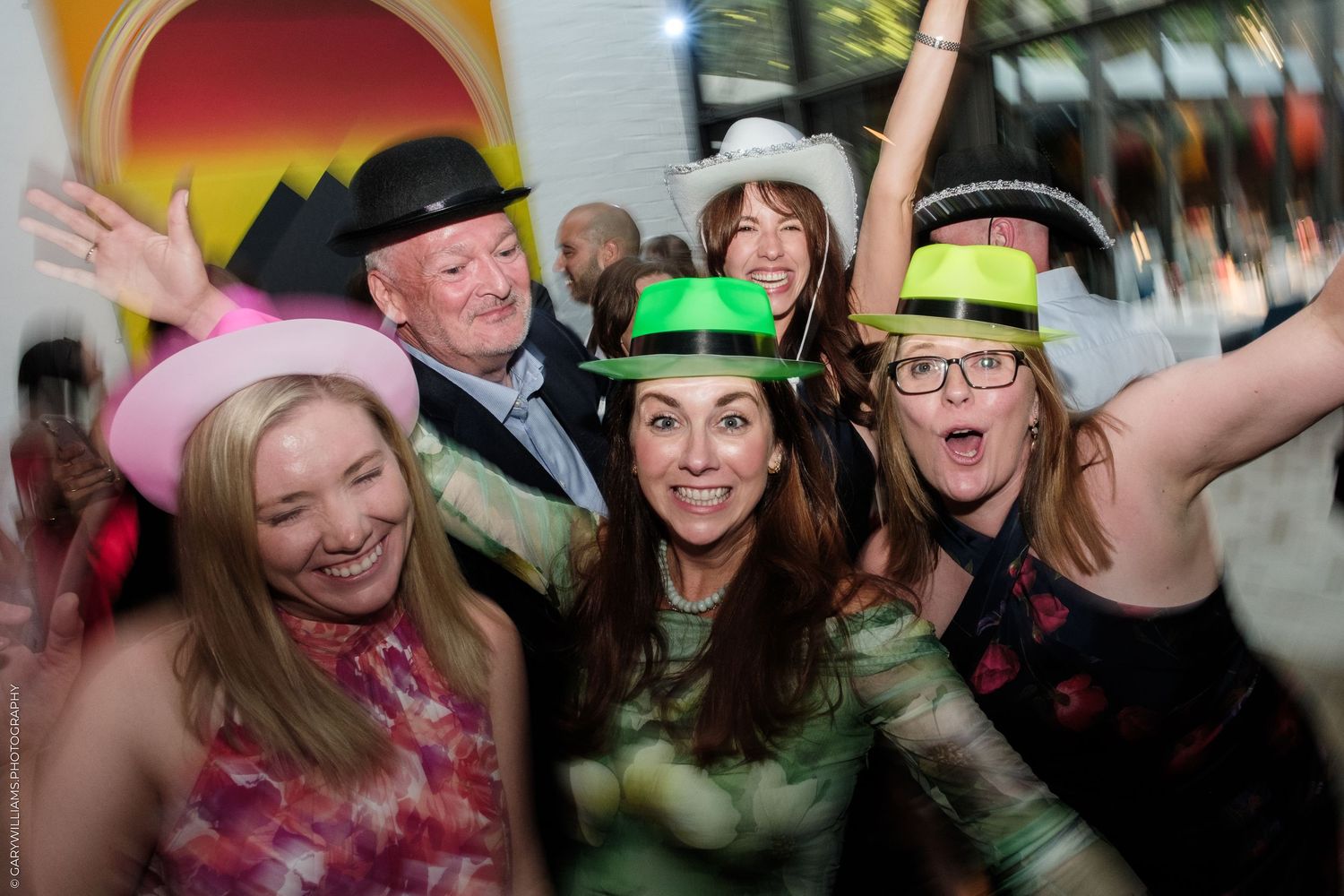 Group of five people wearing colorful novelty hats smiling and celebrating at a lively party event.