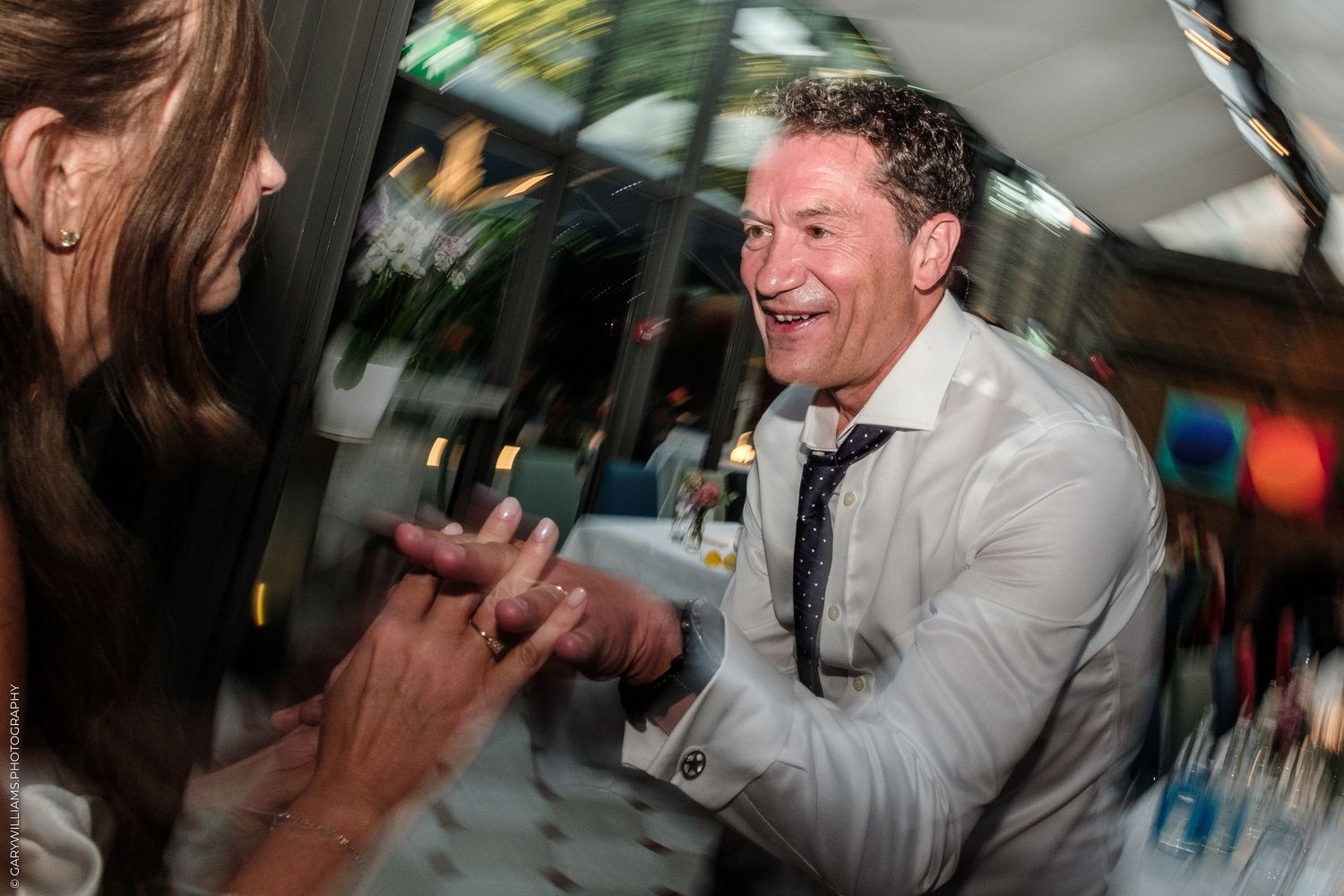 A laughing man in a white shirt and tie enjoys a lively celebration at an indoor event.