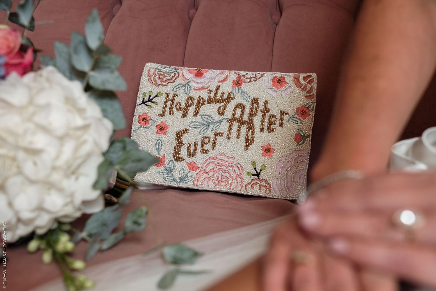 A floral "Happily Ever After" card rests beside a white wedding bouquet on a pink velvet chair.