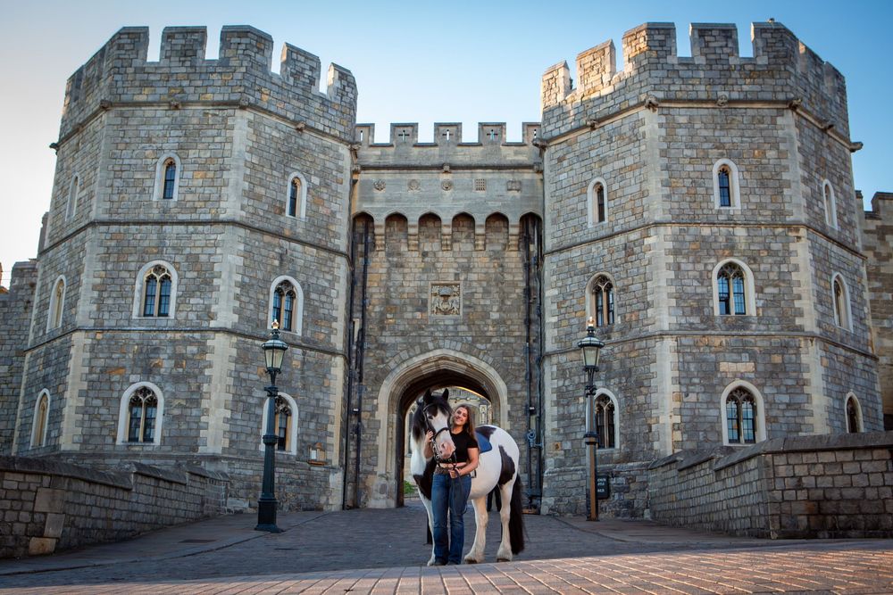 Person with a horse standing at the grand entrance of Windsor Castle, a historic medieval stone fortress.
