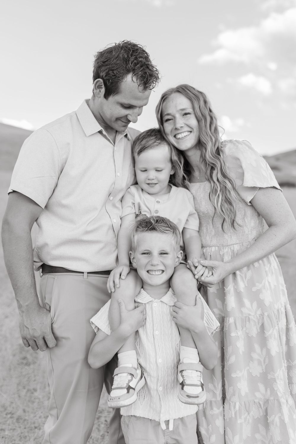 Black and white family portrait of parents with two young children smiling outdoors in a field.