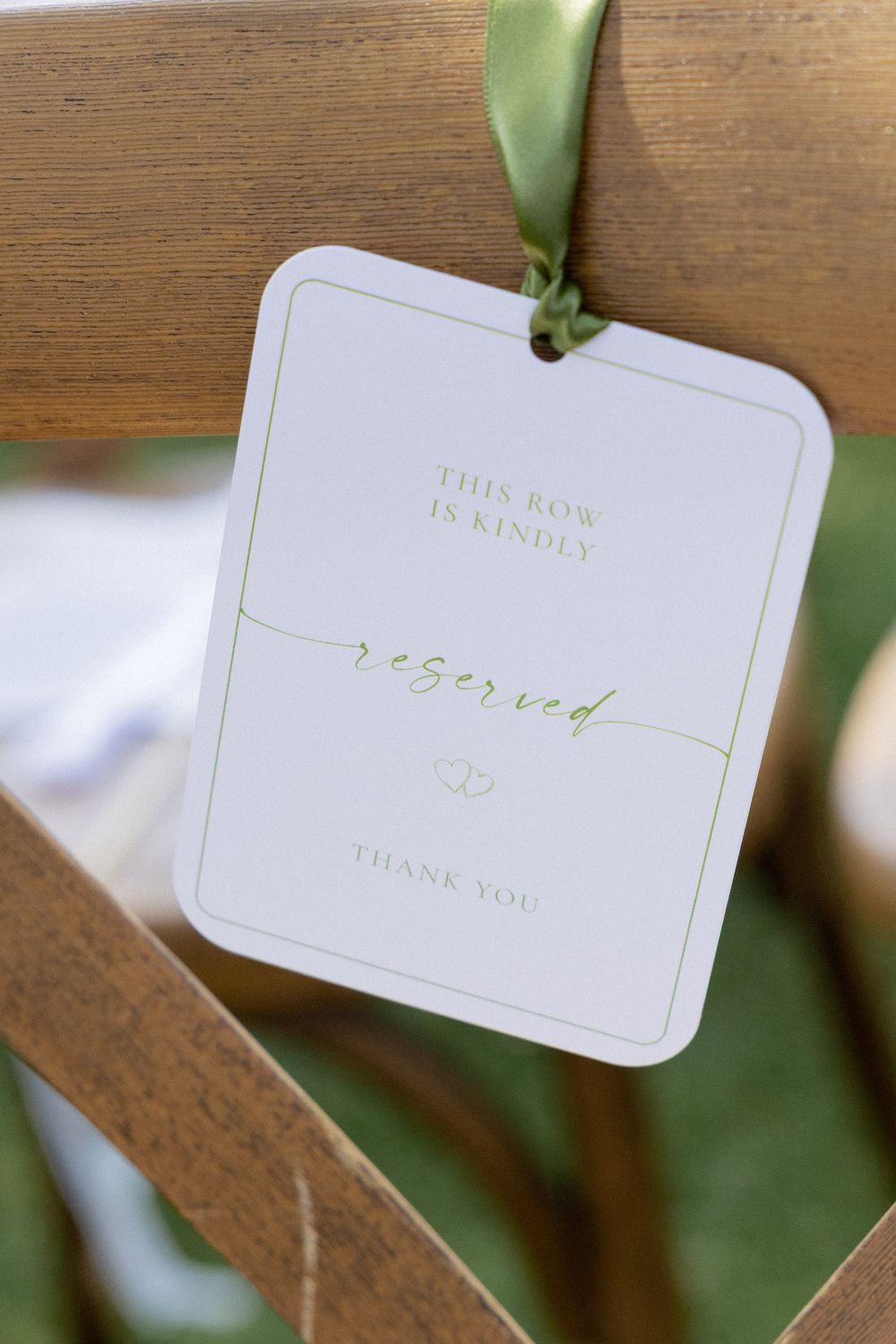 Elegant reserved row sign hanging on wooden chair with green ribbon at outdoor wedding.