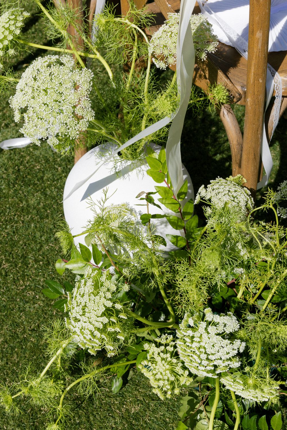 White Queen Anne's lace and green foliage wedding aisle decorations on grass.