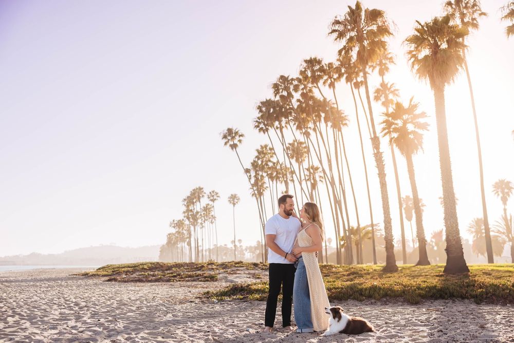 Couple embracing on a sunny beach with tall palm trees in Santa Barbara, California during golden hour. Santa Barbara maternity photos