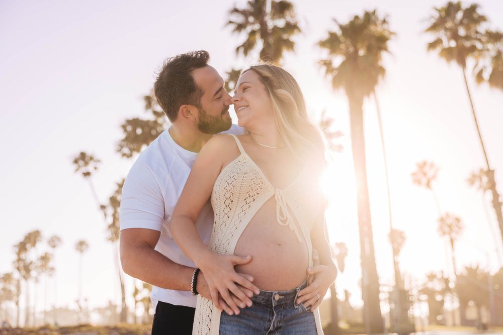 Couple embracing outdoors with pregnant belly, palm trees and golden sunlight in the background. Planning Guide