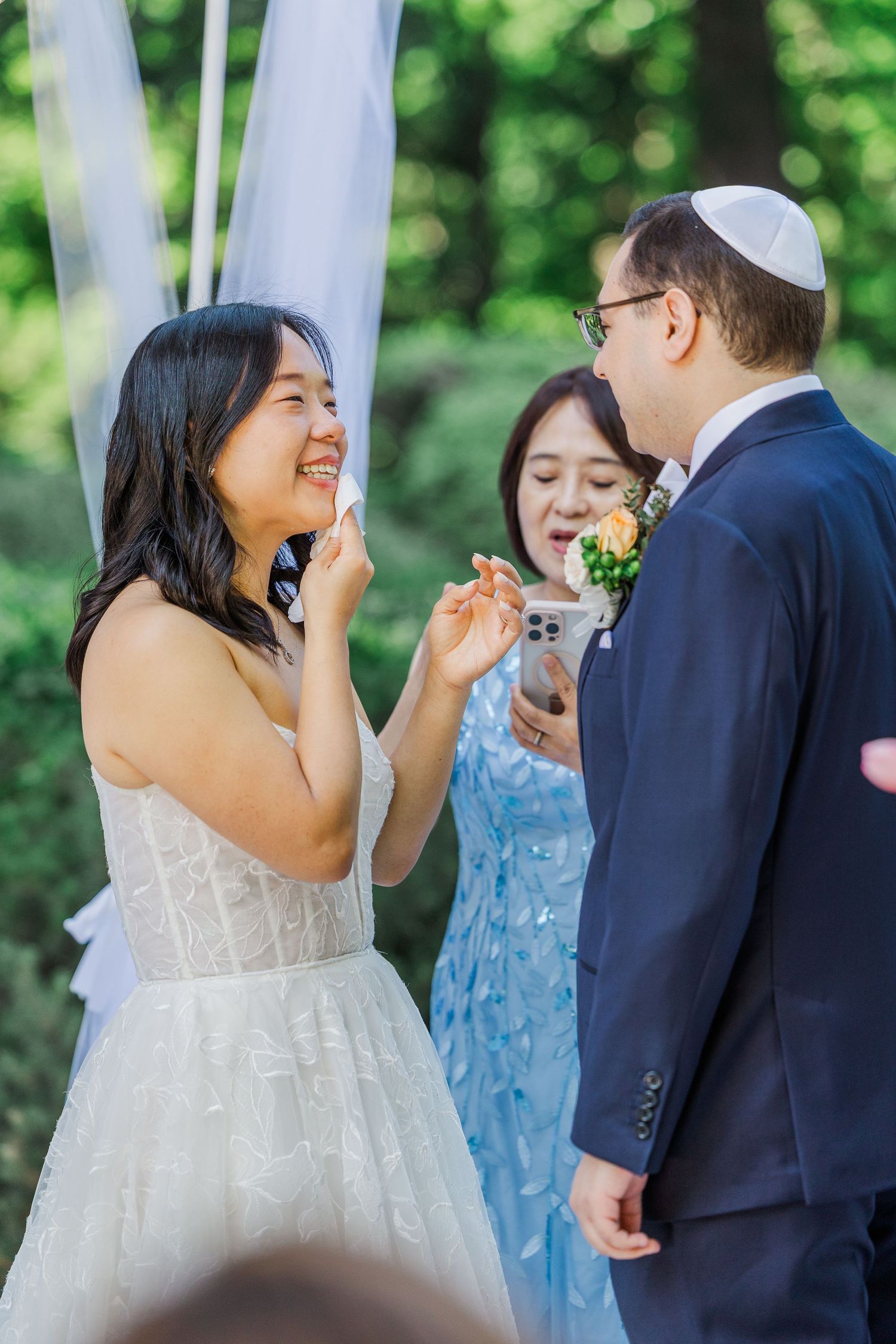 Bride and groom sharing a joyful moment during outdoor wedding ceremony with officiant in blue dress.
