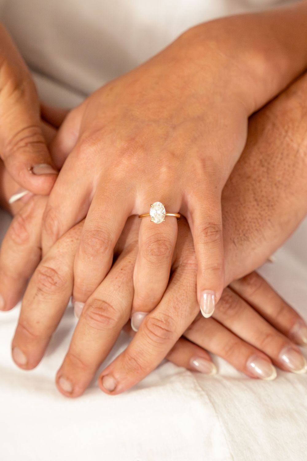 Engagement photo of fiance's hands overlapping. Engagement ring is a beautiful oval diamond set in yellow gold