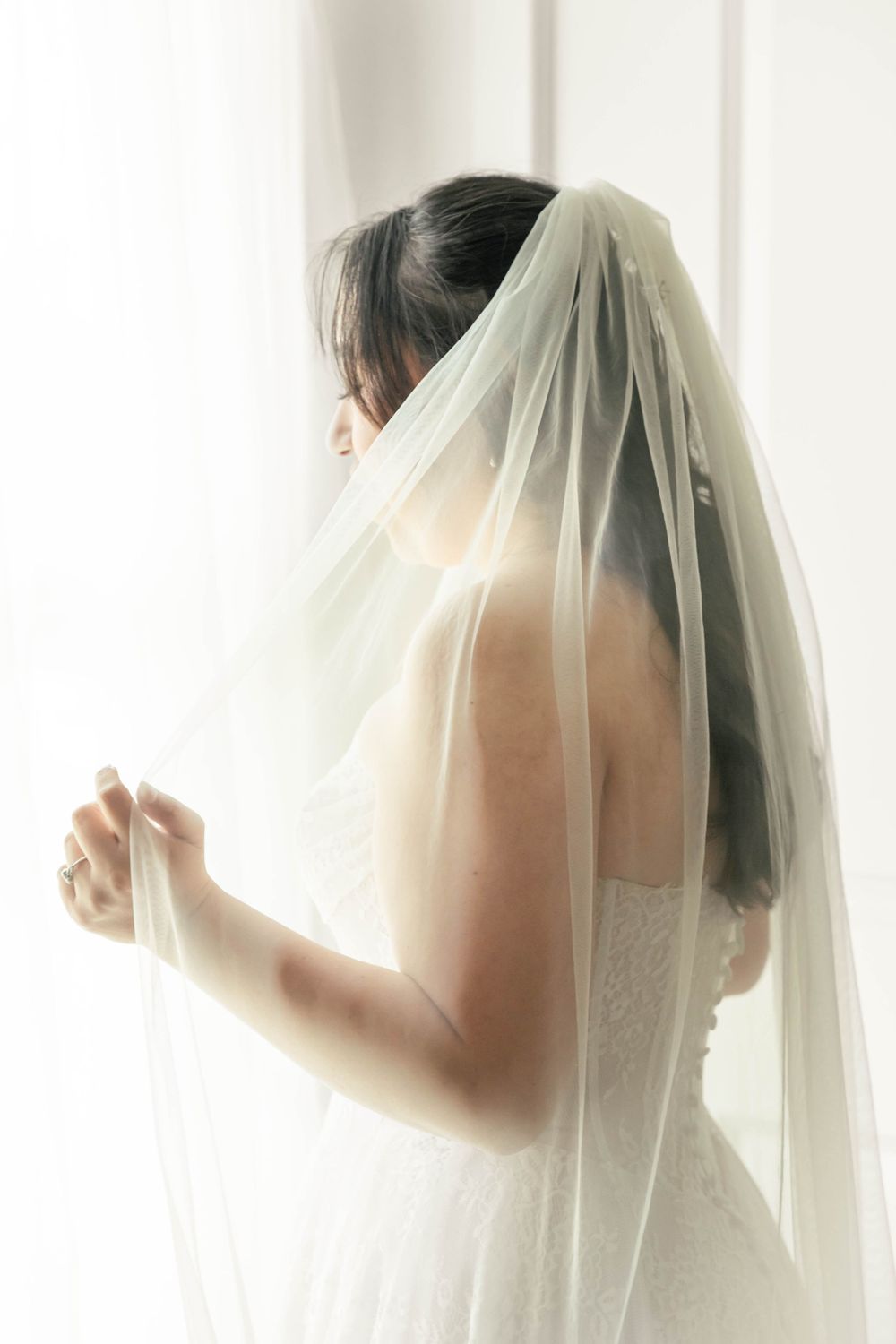 Bridal portrait, bride standing in natural light at a window holding out her veil