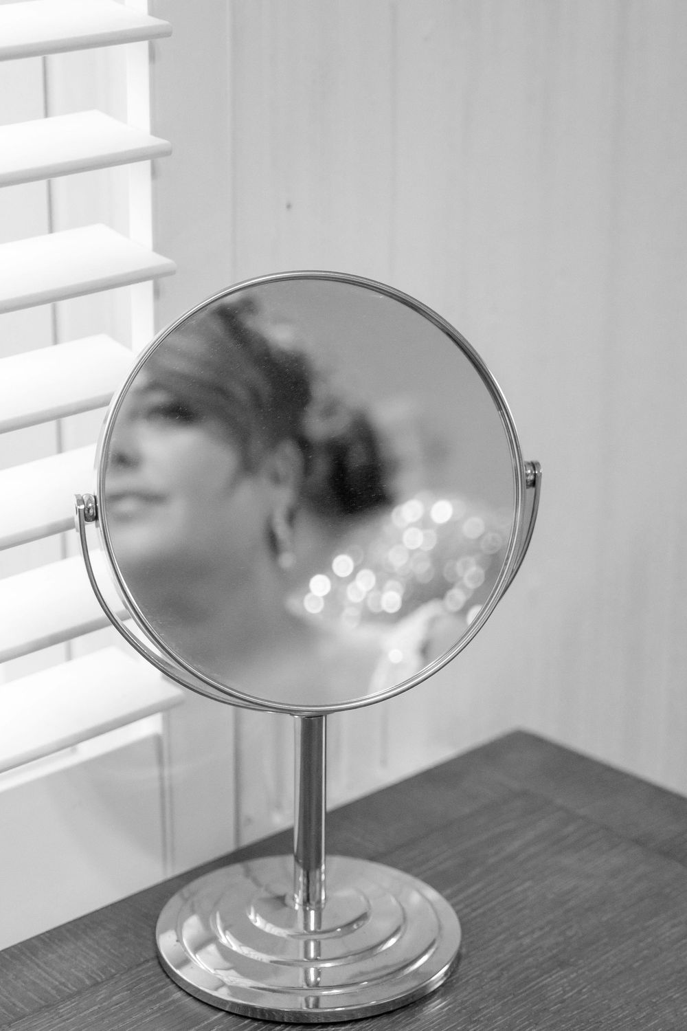 Bride getting ready shot, looking at the bride through an oval mirror in B&W