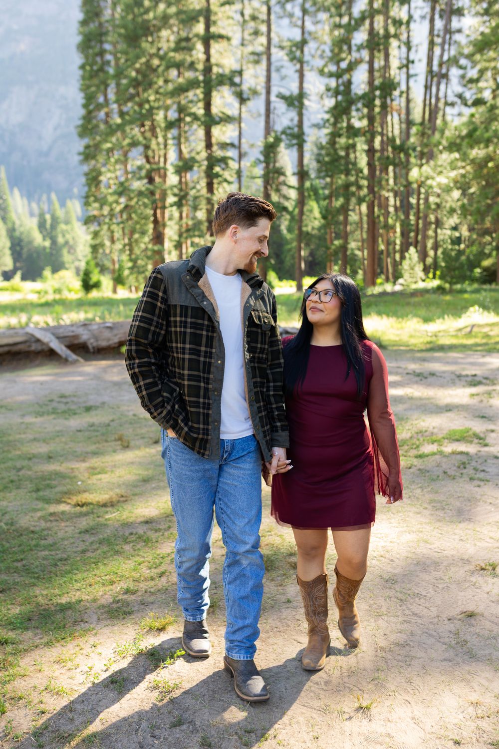 Couple holding hands and smiling at each other while walking on a forest path in Yosemite National Park.