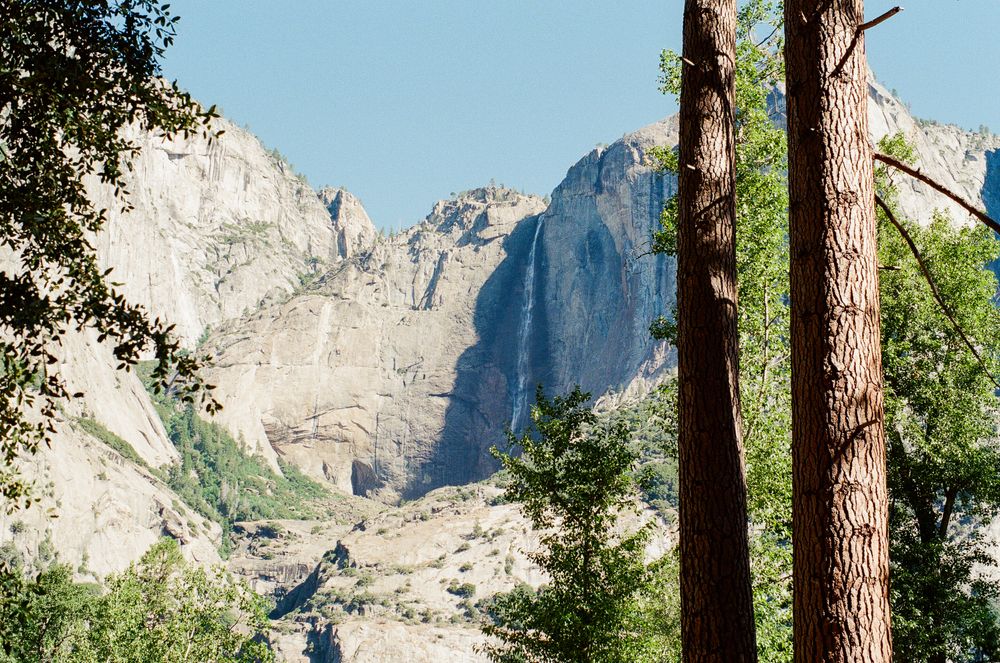 Towering granite cliffs and lush pine trees frame a stunning mountain landscape under a clear blue sky in Yosemite National Park.