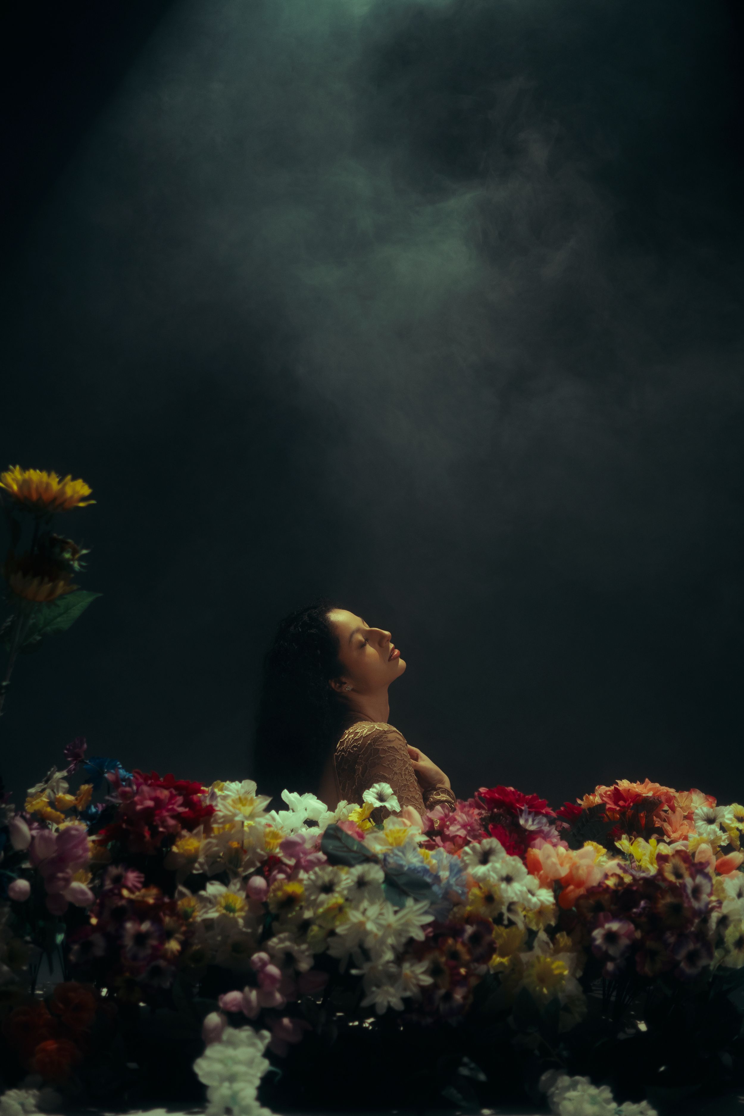 Moody fine art portrait of a woman surrounded by colorful flowers against a dark cinematic background