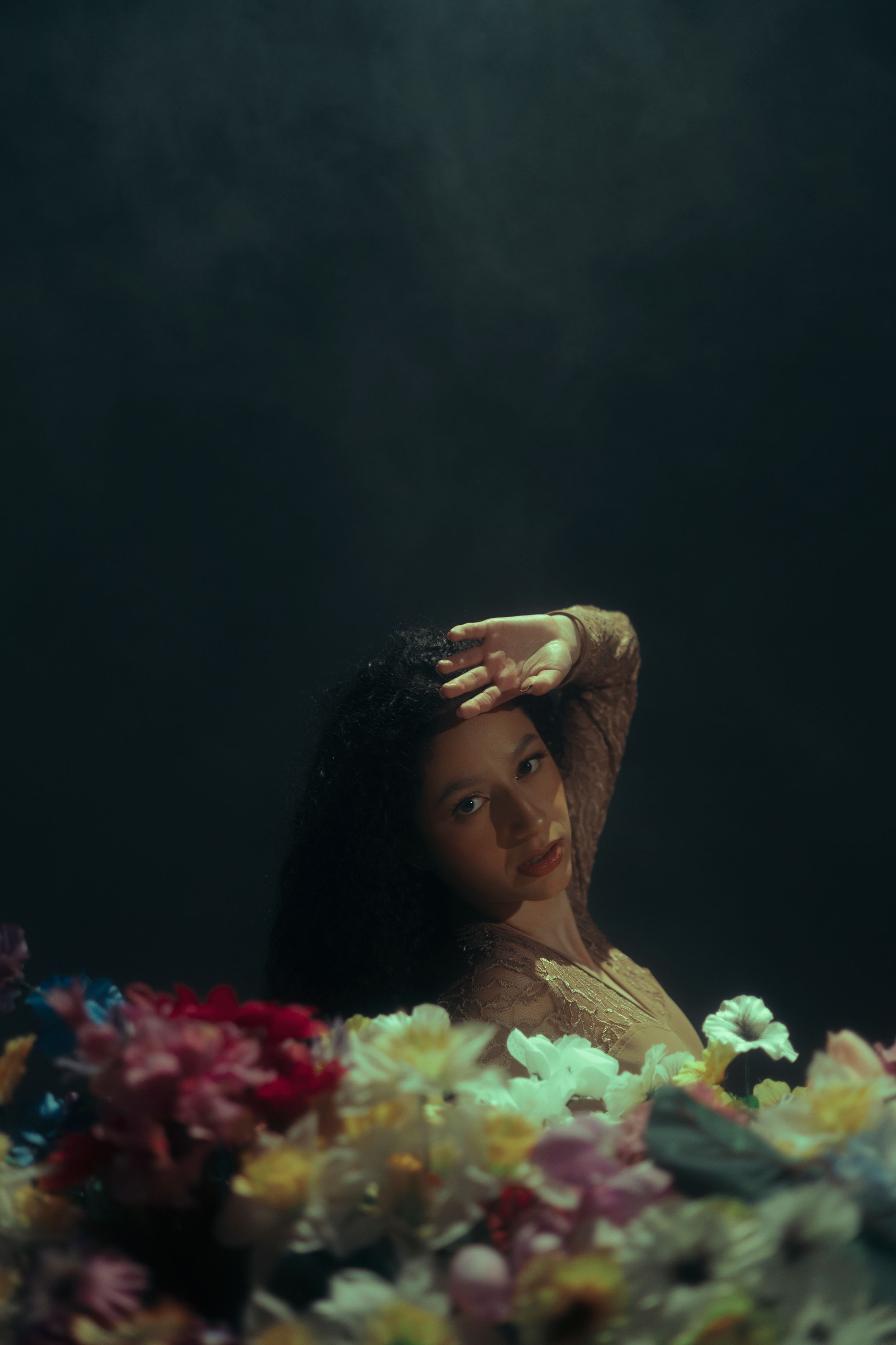 Dark editorial portrait of a woman surrounded by flowers with dramatic cinematic lighting