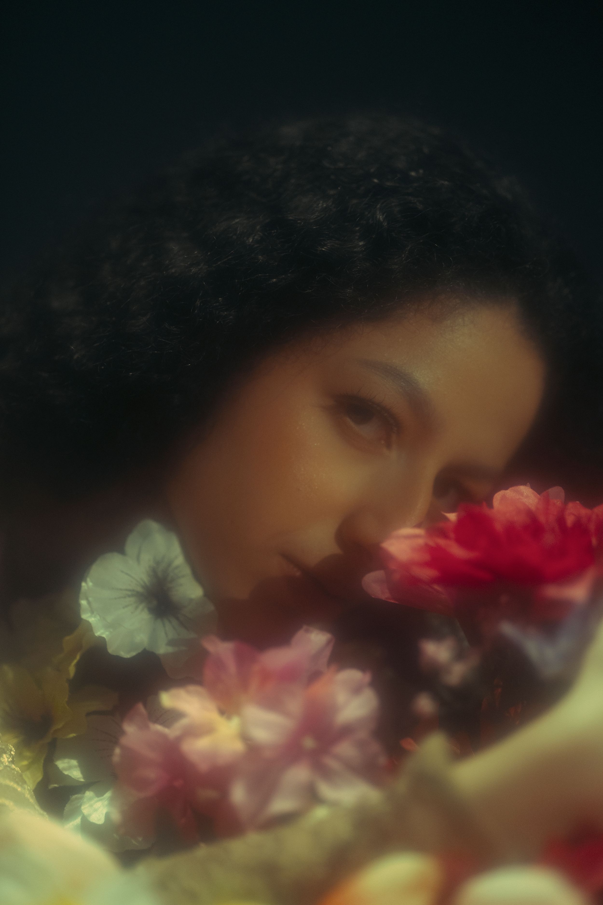 Dreamlike close-up portrait of a woman resting among colorful flowers with soft cinematic focus