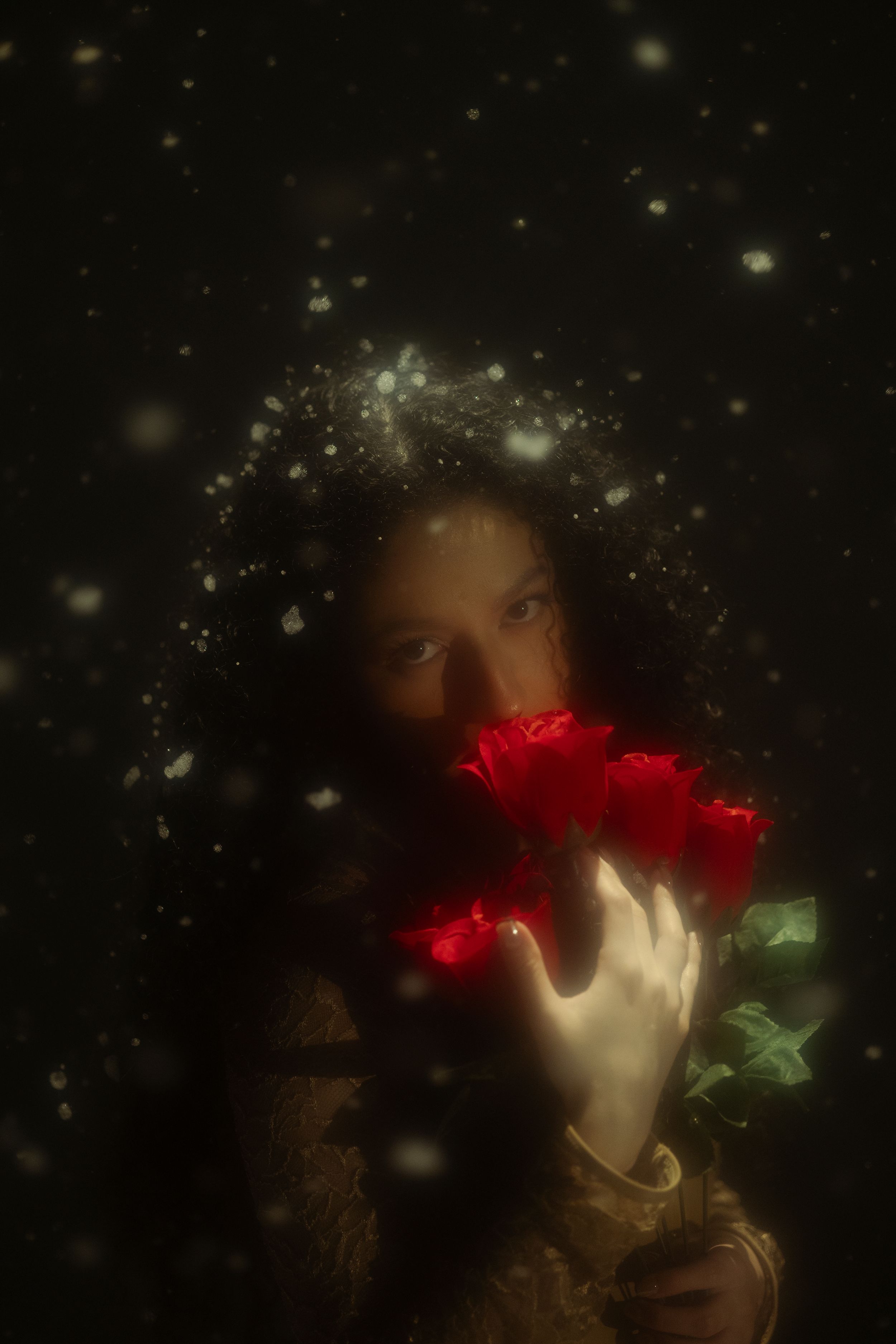Moody fine art portrait of a woman holding red flowers against a dark background