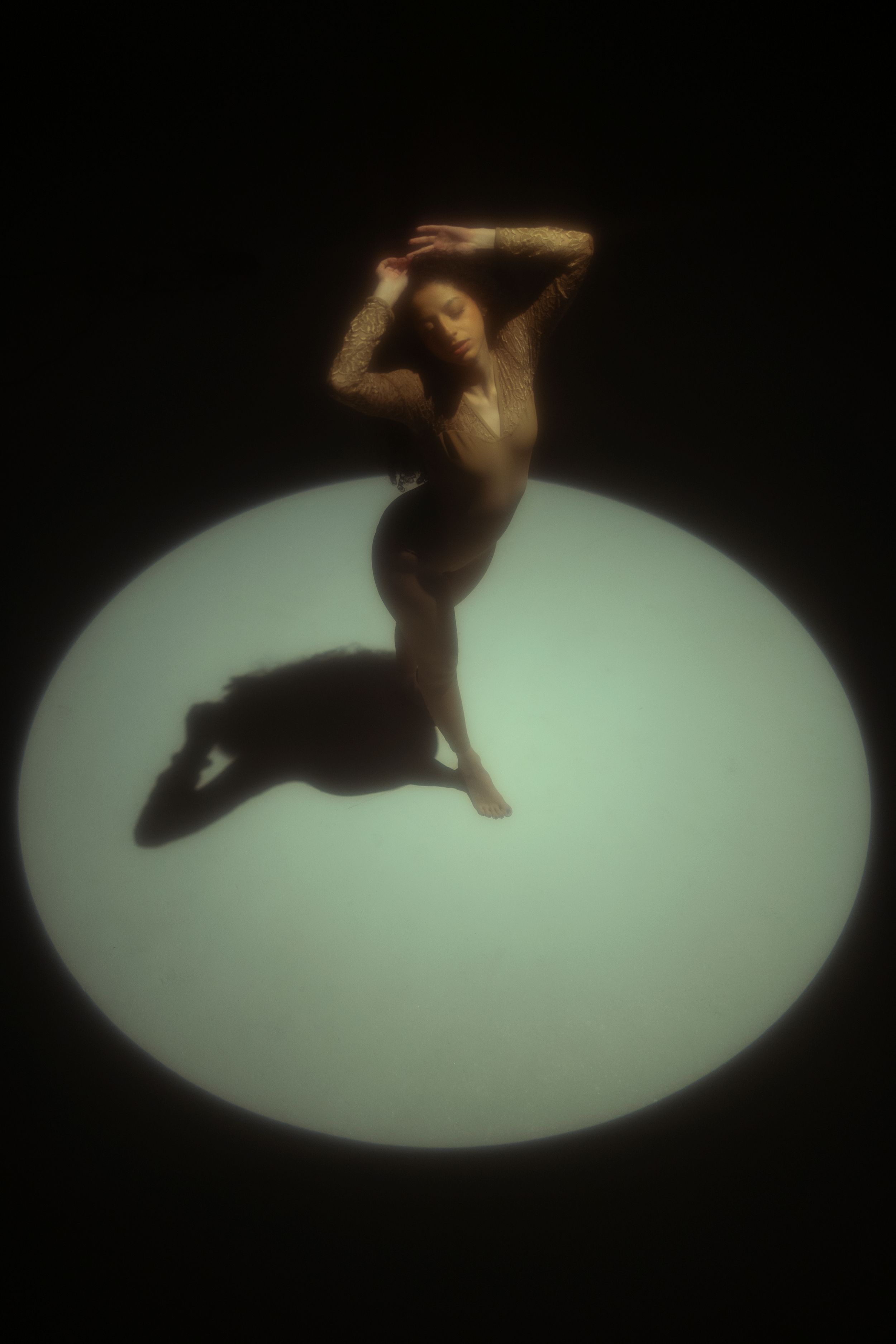 Conceptual full-body portrait of a woman posing inside a circular spotlight in a dark studio