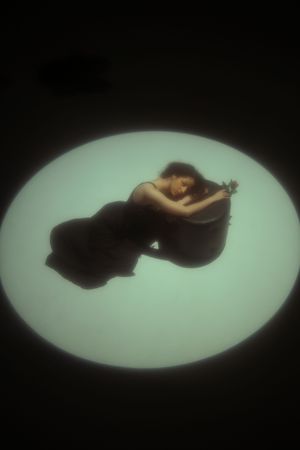 Conceptual overhead portrait of a woman lying in a circular spotlight against a dark background
