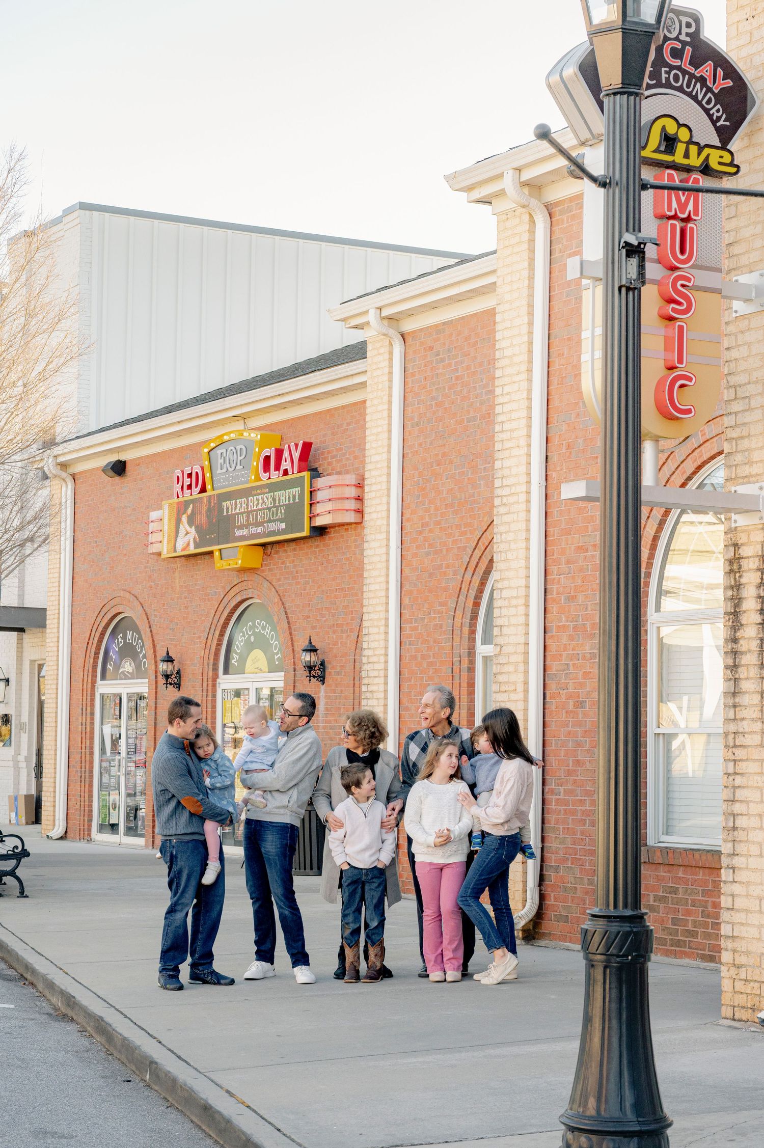 Multi-generational family gathered outside Red Clay Live Music venue on a brick sidewalk in a small town.