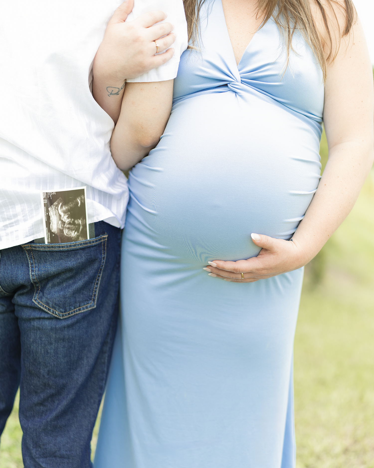 Couple maternity photo showing baby bump in blue dress with partner holding ultrasound photo.