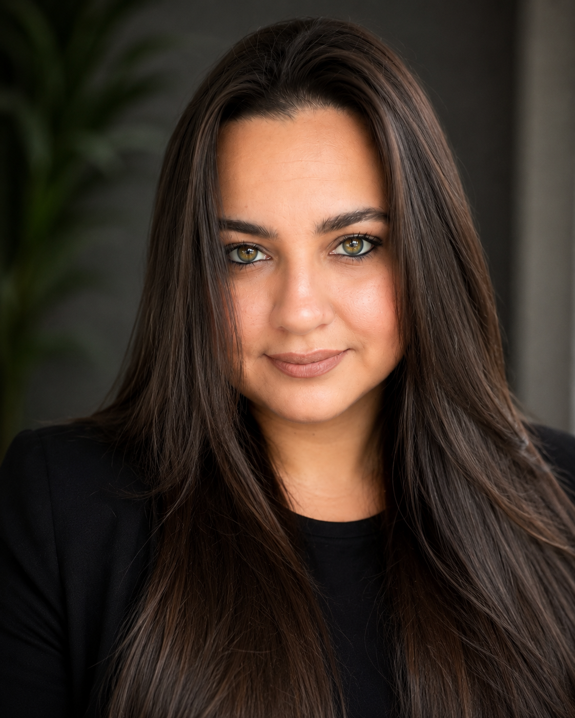 Professional headshot of a young woman with long dark hair and green eyes wearing a black blazer.