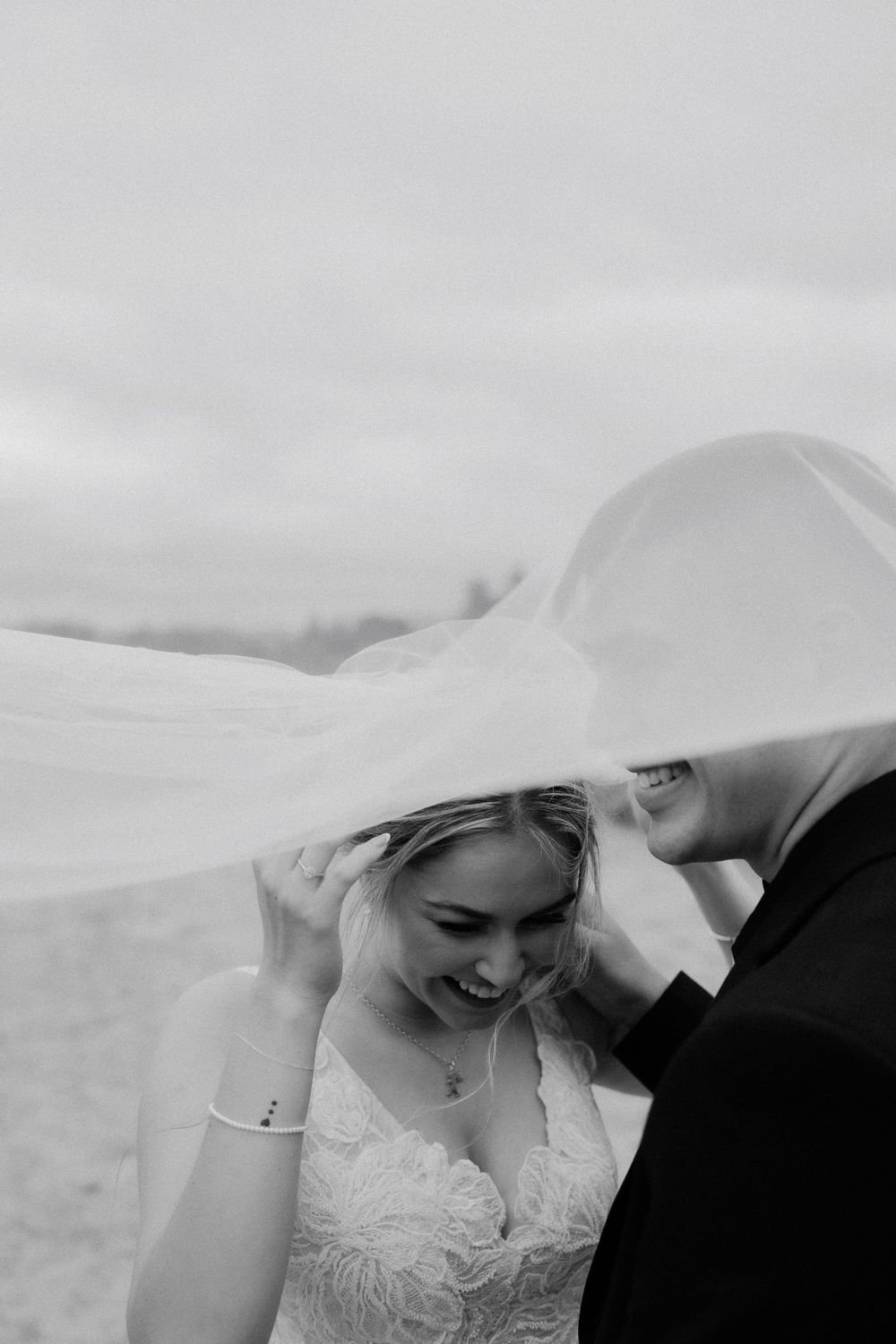 A romantic black and white wedding photo showing a couple under a flowing veil in an intimate moment.