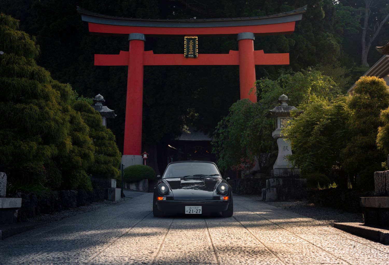 Two black Porsche 911s parked on a Japanese street with a traditional red temple gate in the background.