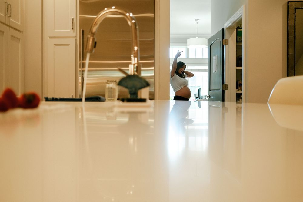 Low-angle view of a glossy white kitchen countertop with a modern faucet and a person visible in the background.